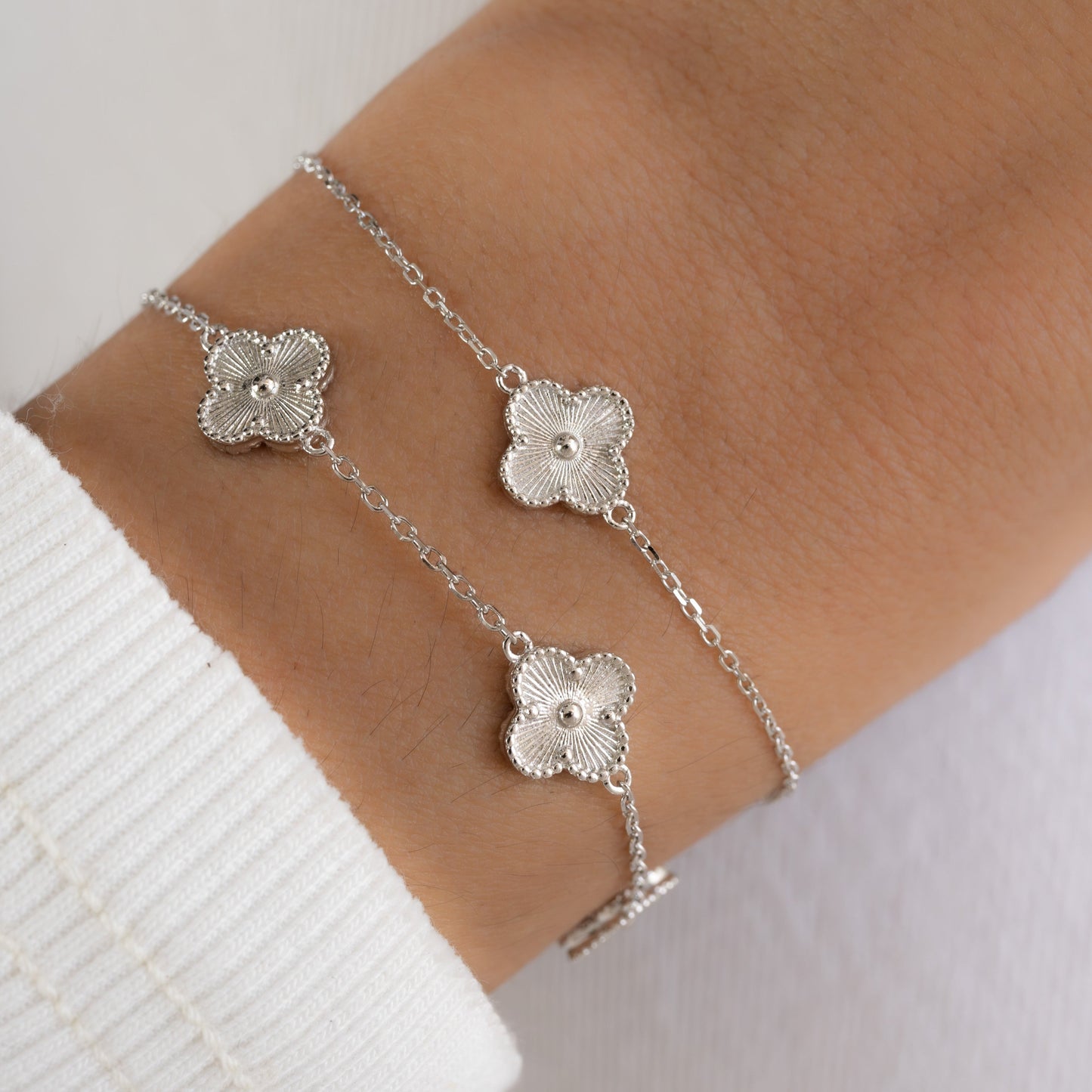 A model wearing two bracelets, one of a four leaf clover bracelet in silver and with a charm bracelet with five four clover leaf charms.