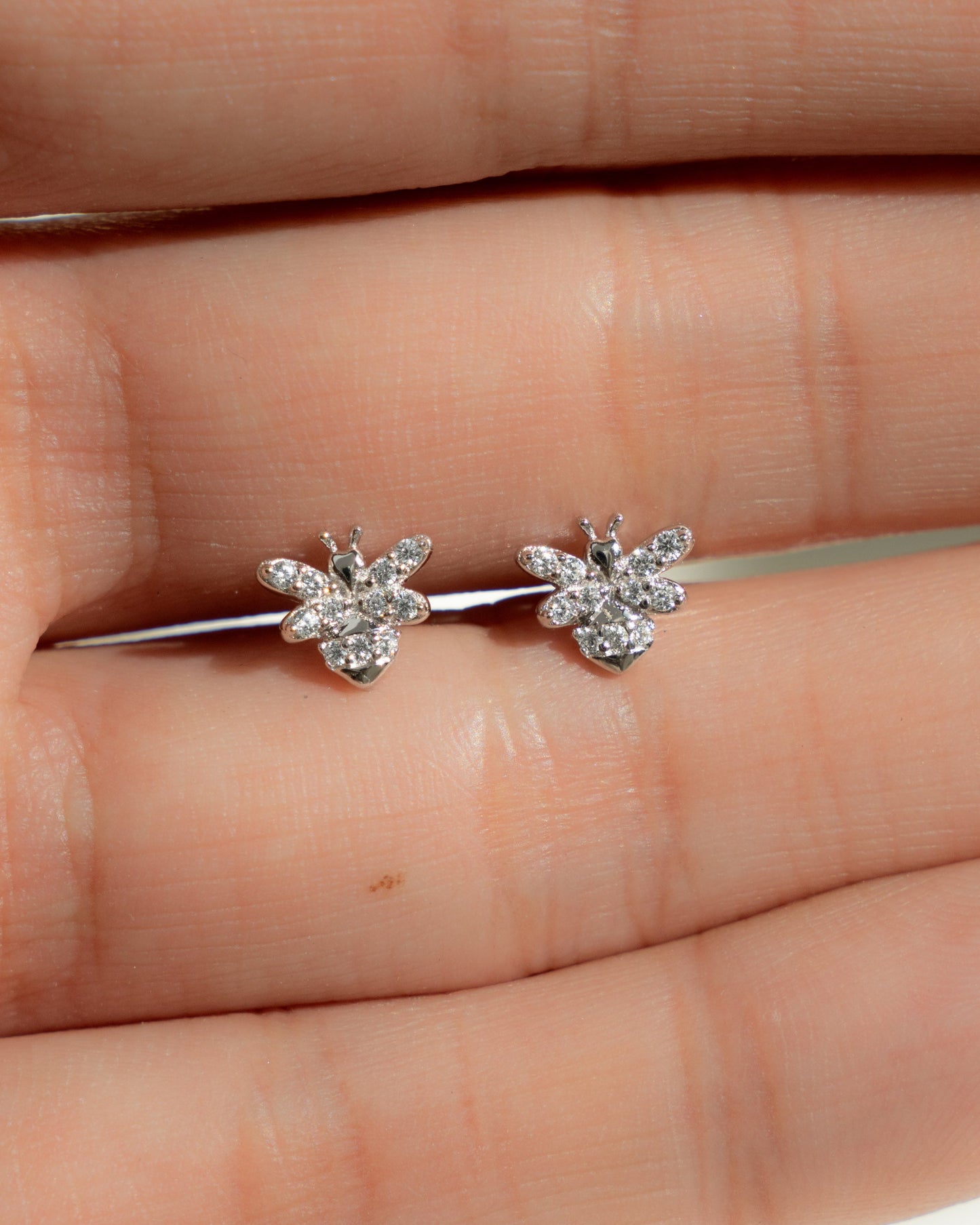 closeup image of silver stud earrings with a bee earring design