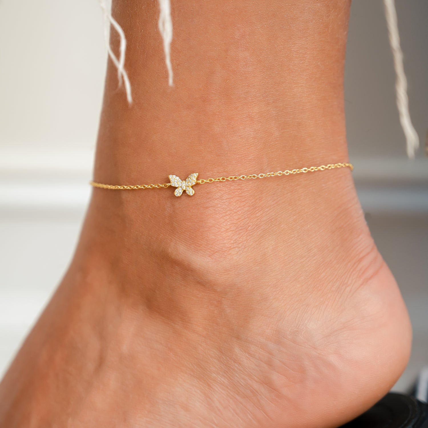 Model wearing dainty gold butterfly charm anklet