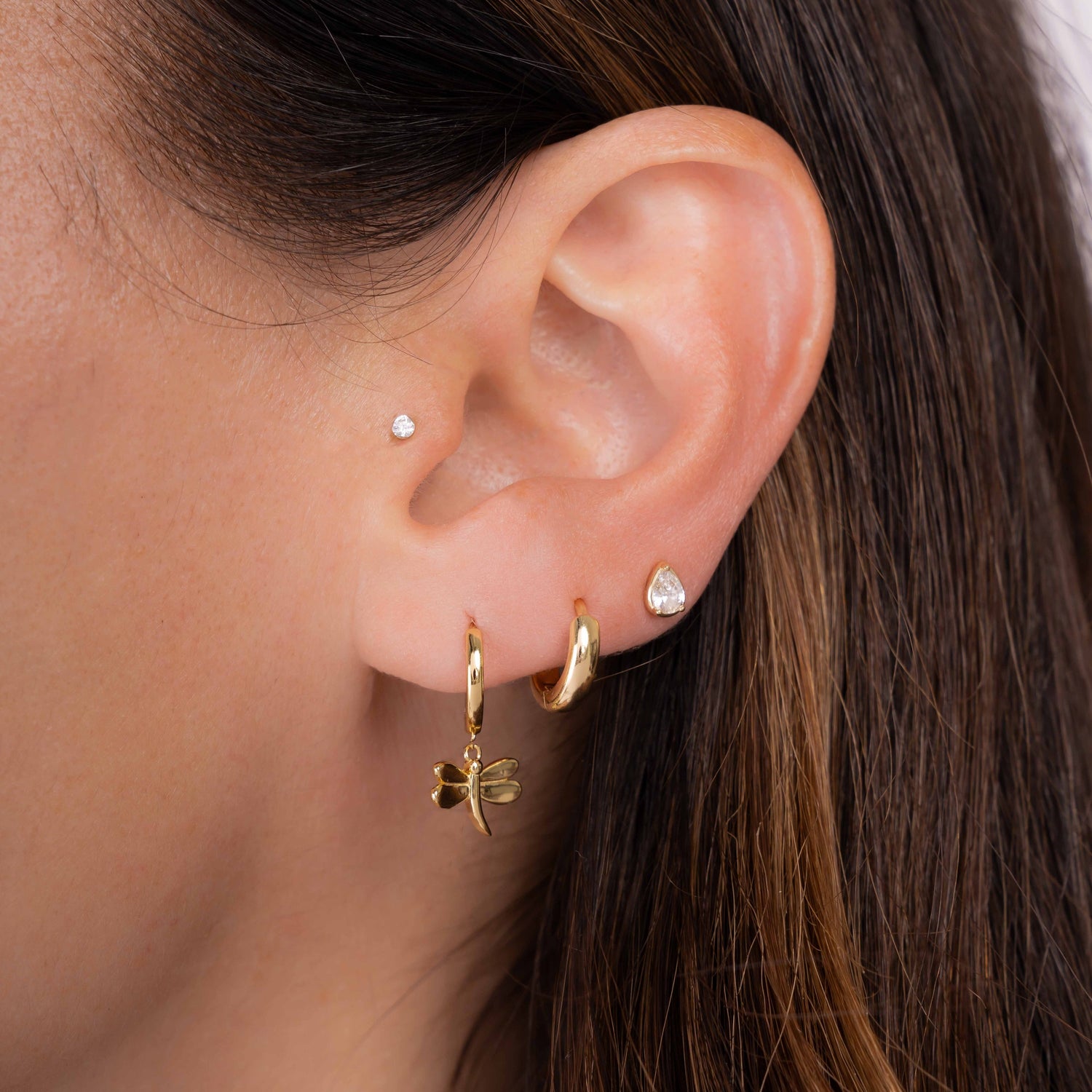 Dragonfly earrings worn on model with small huggie hoop and pear studs.
