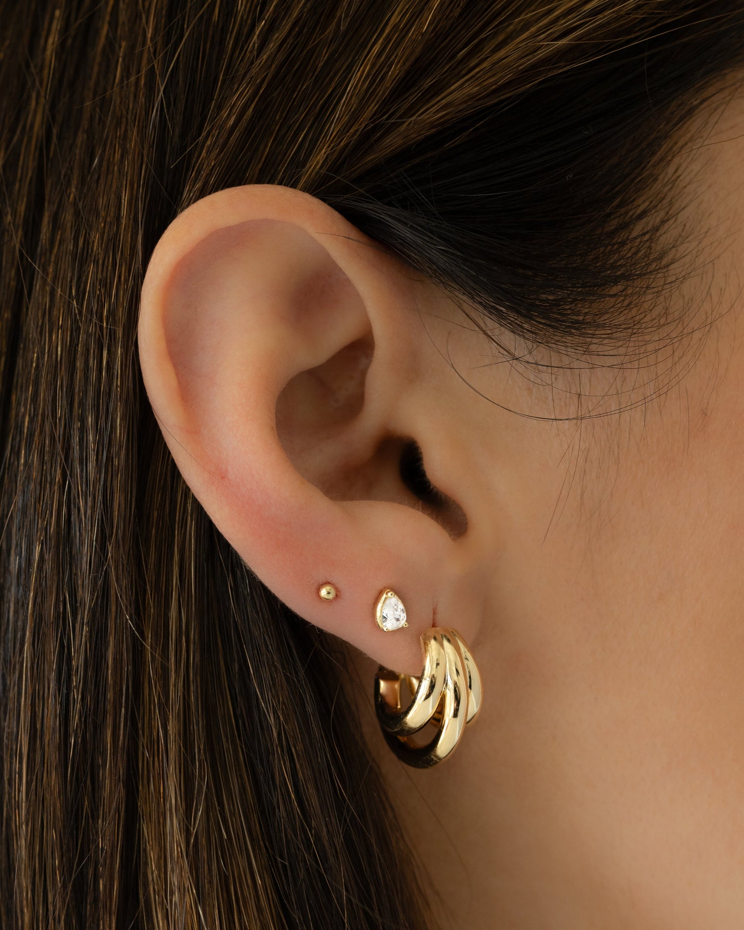 Model wearing gold triple hoop statement earrings, a gold diamond pear stud and a gold ball stud
