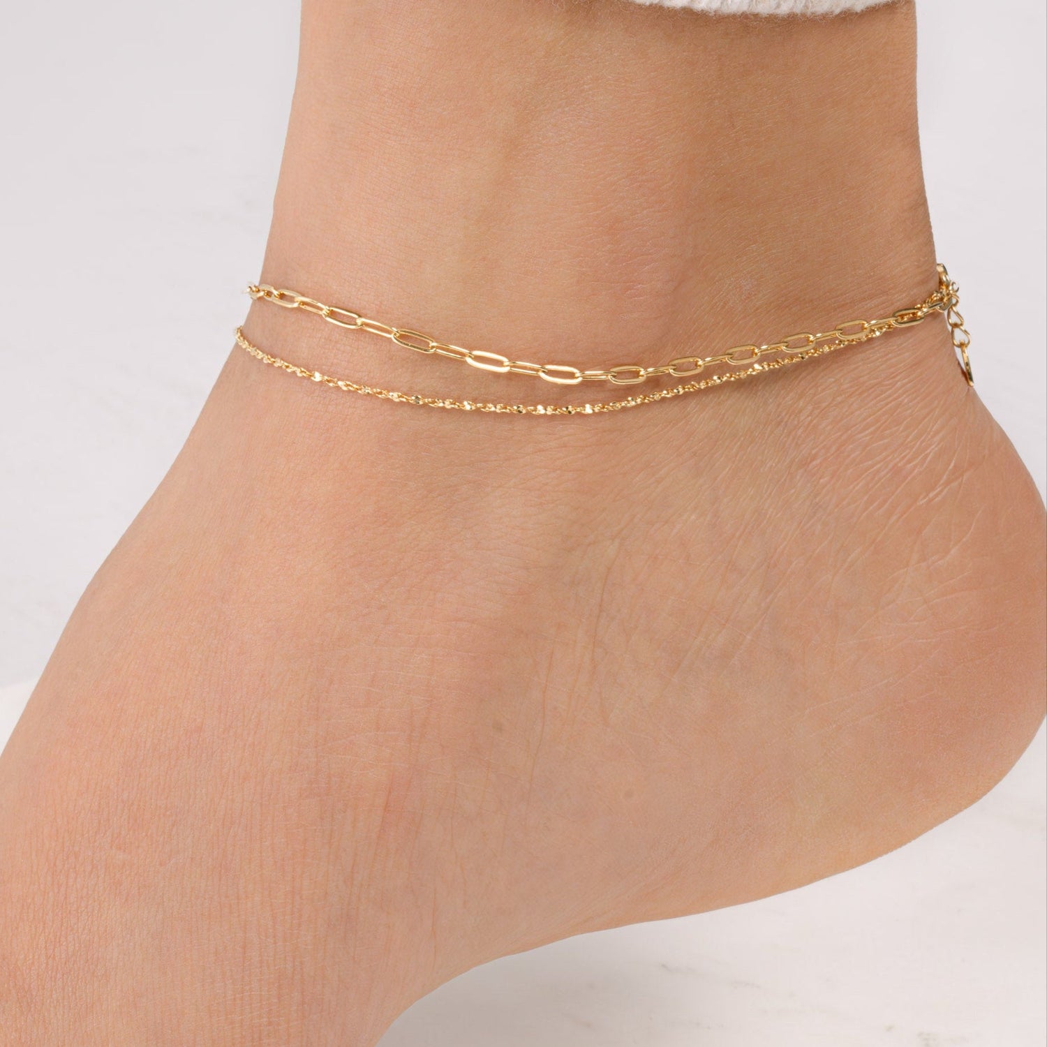 Model wearing a dainty gold ankle bracelet set