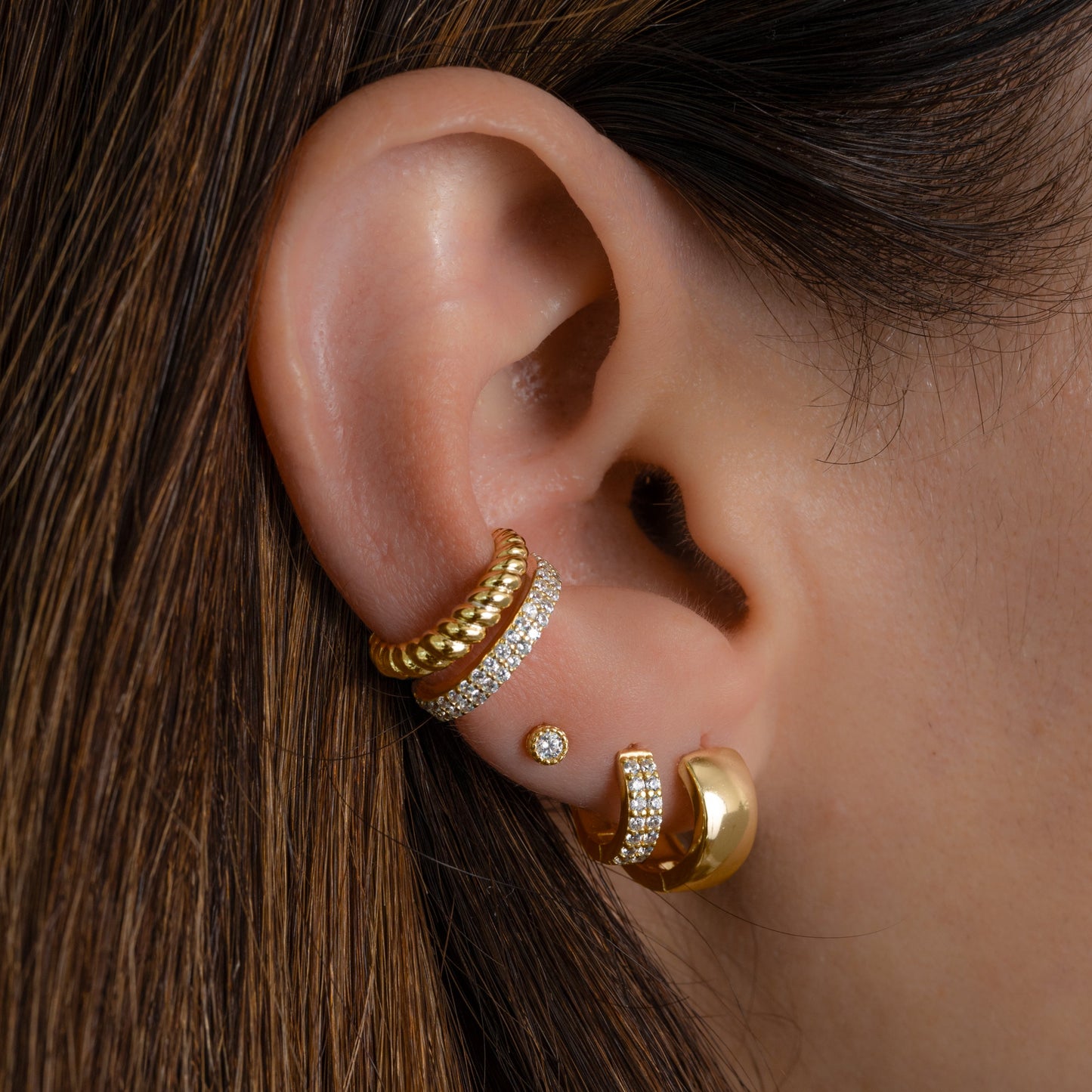Model wearing gold earring stack featuring dainty cubic zirconia ear cuff