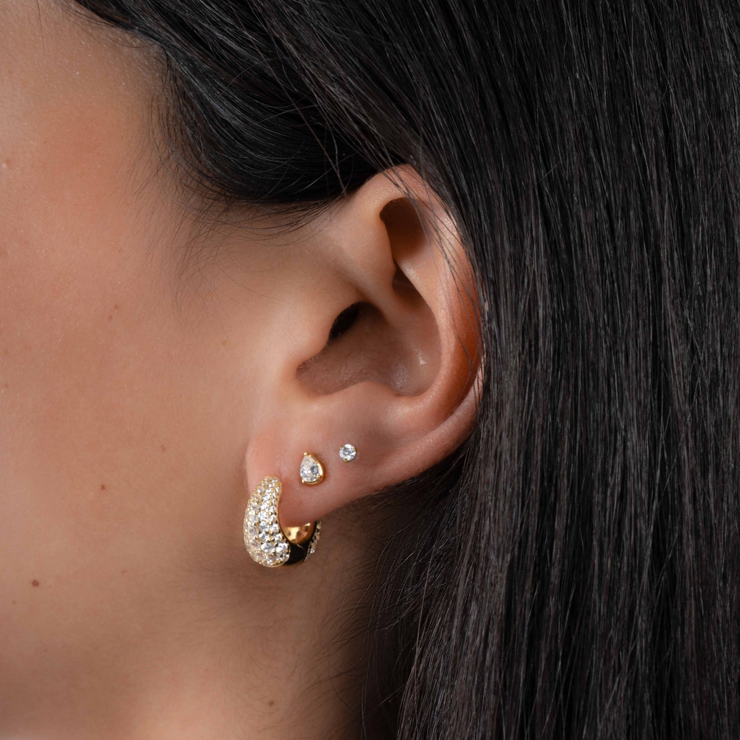 Model wearing diamond earrings featuring small gold huggie hoops