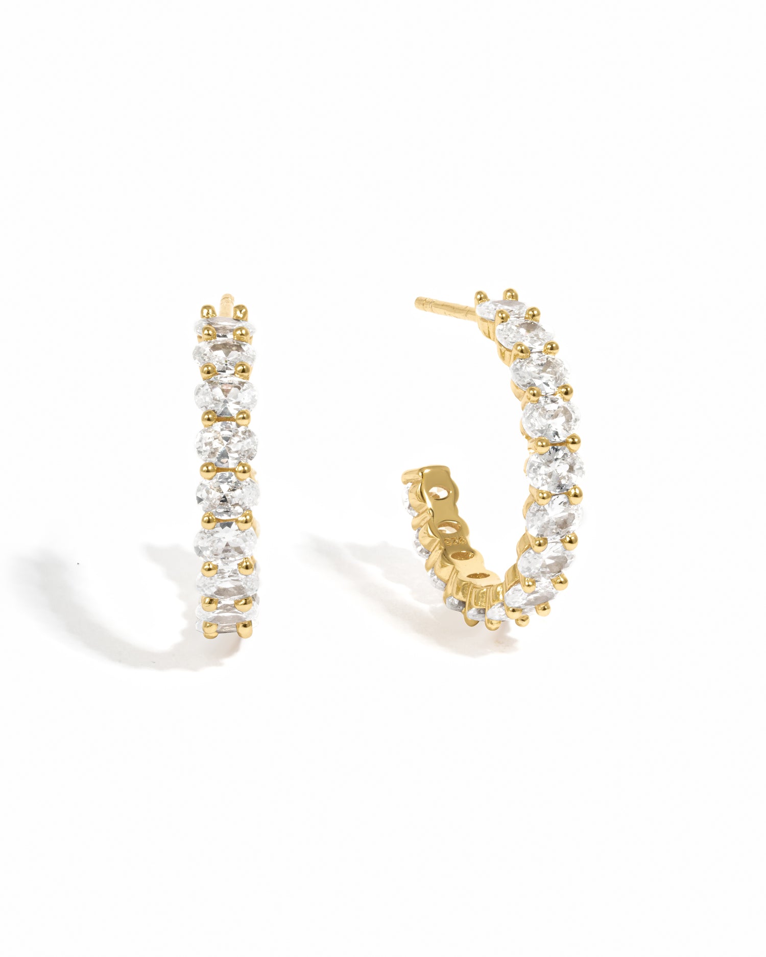 A pair of oval studded hoop earrings made with cubic zirconia, displayed against a white background.