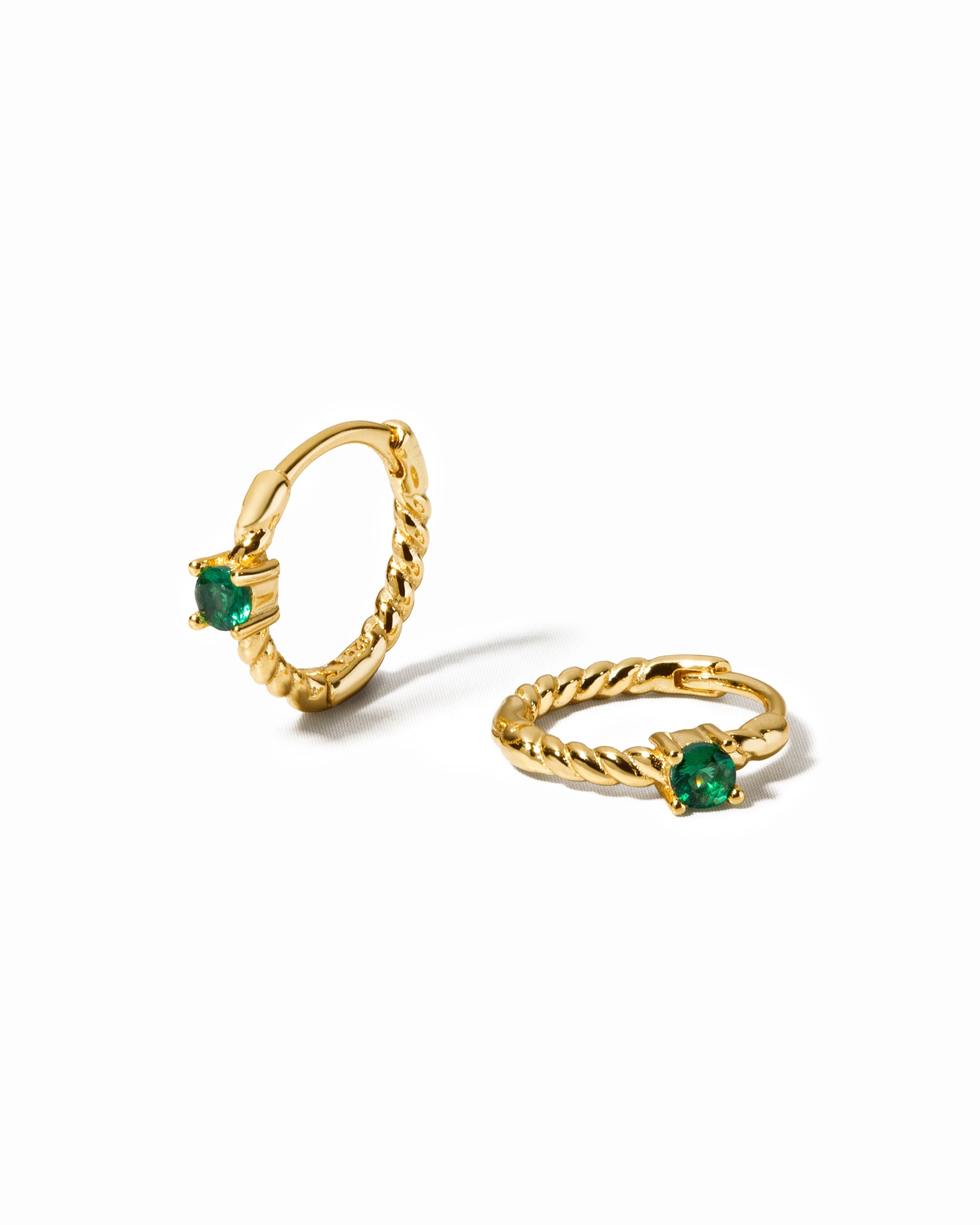 Small hoop earrings with a spiral design with emerald gemstones on a white background