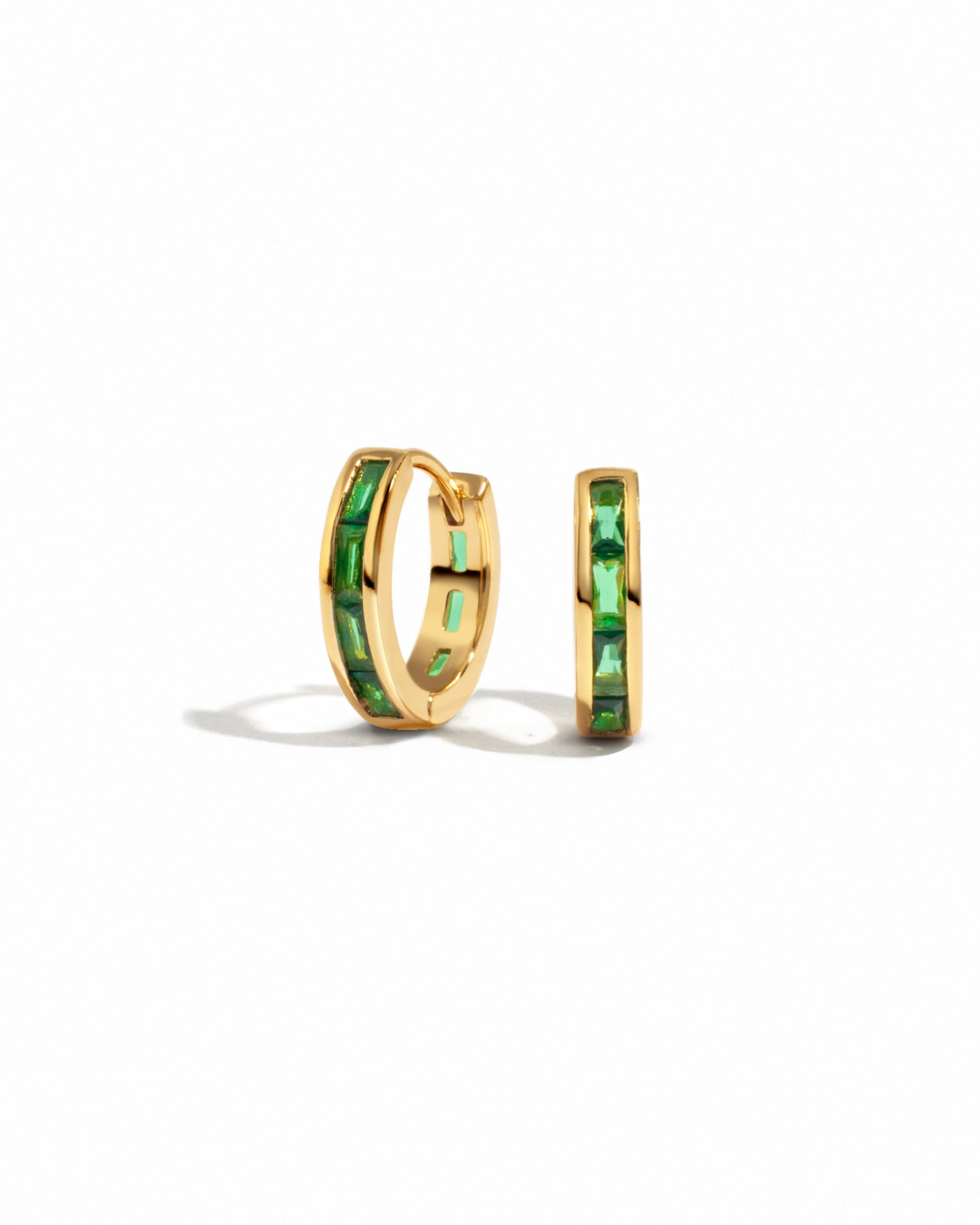 A pair of emerald baguette huggie earrings displayed against a white background.
