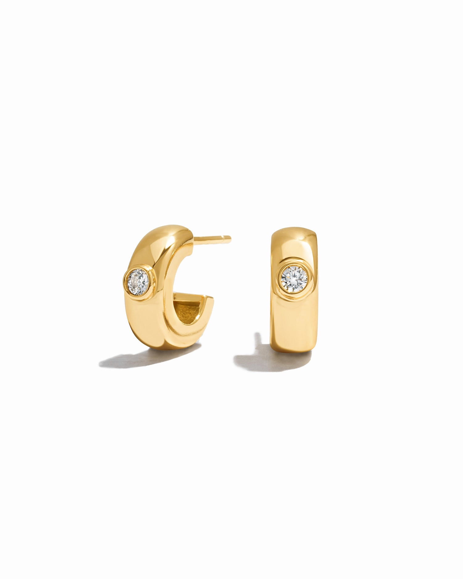 Gold huggie hoops with a bezel set diamond on a white background