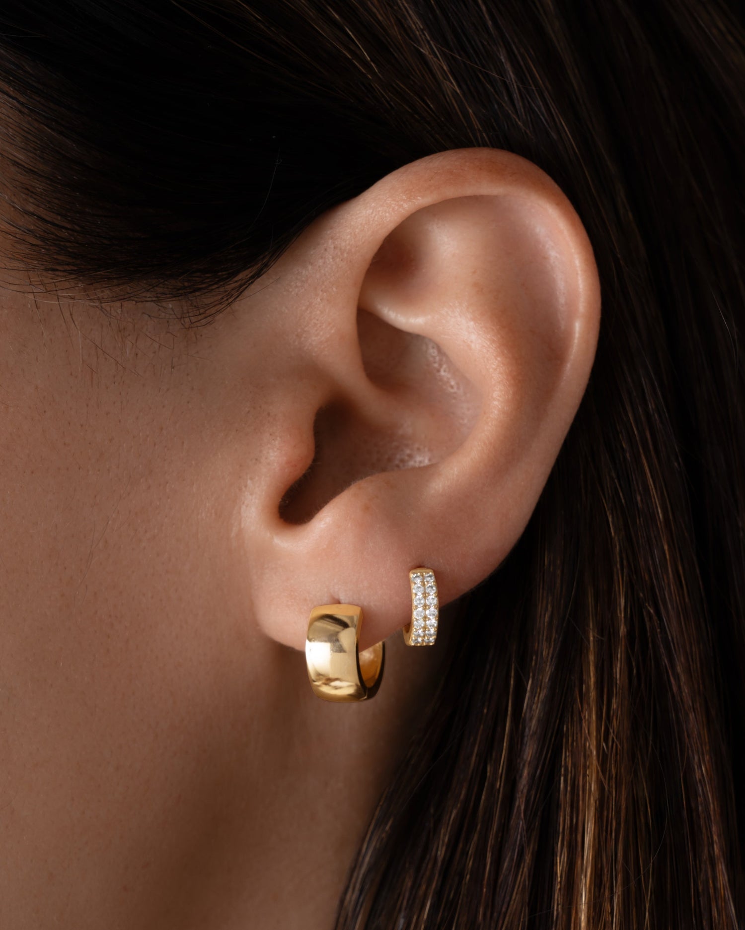 Model wearing gold chunky hoop earrings and two row diamond huggie earring