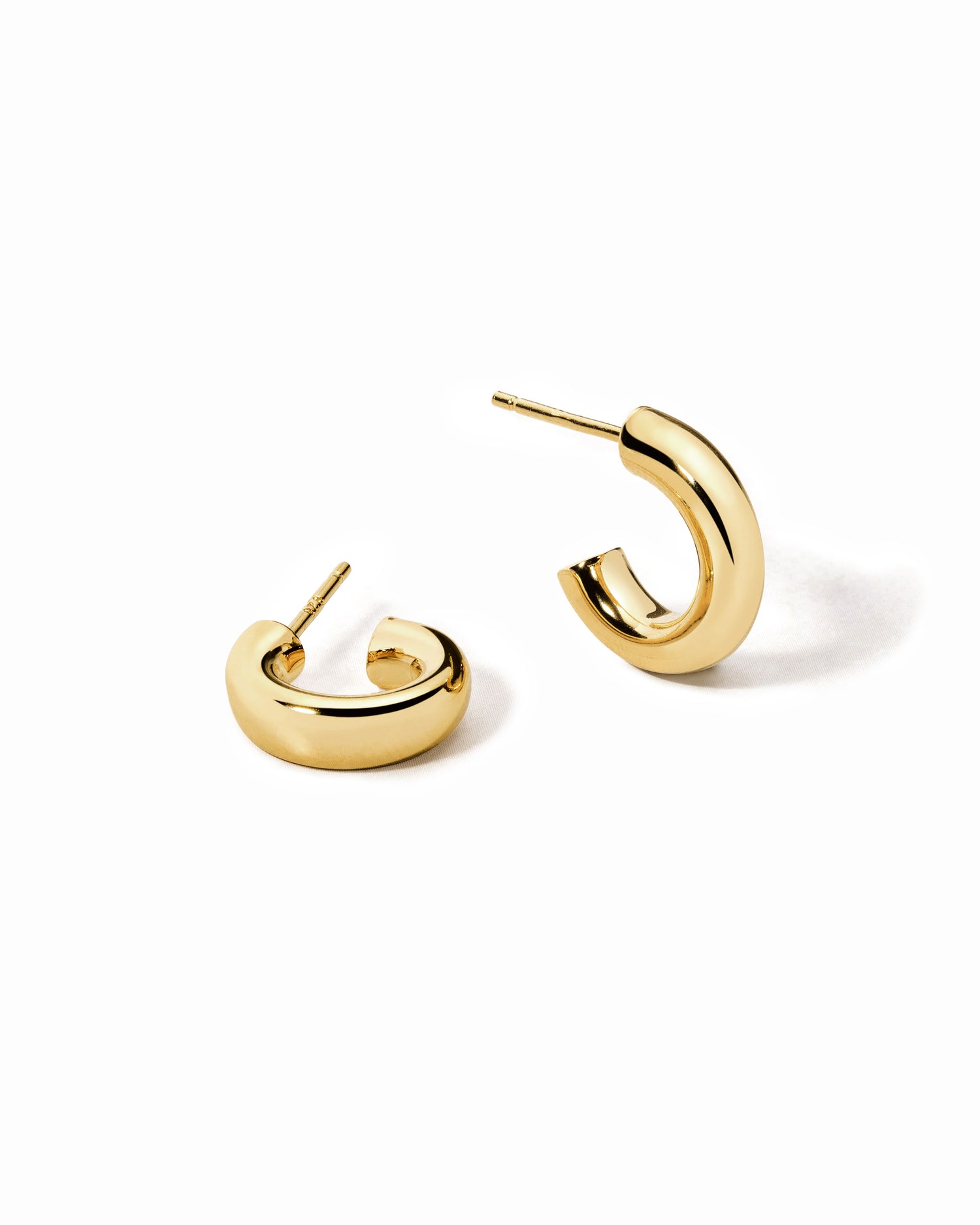 A pair of chunky gold tube hoop earrings on a white surface.