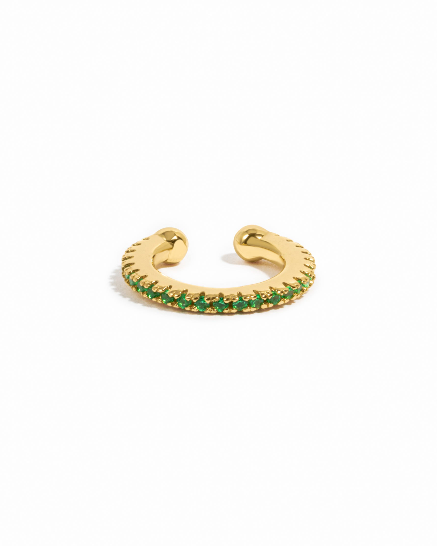Gold ear cuff with emerald green gemstones on a white background