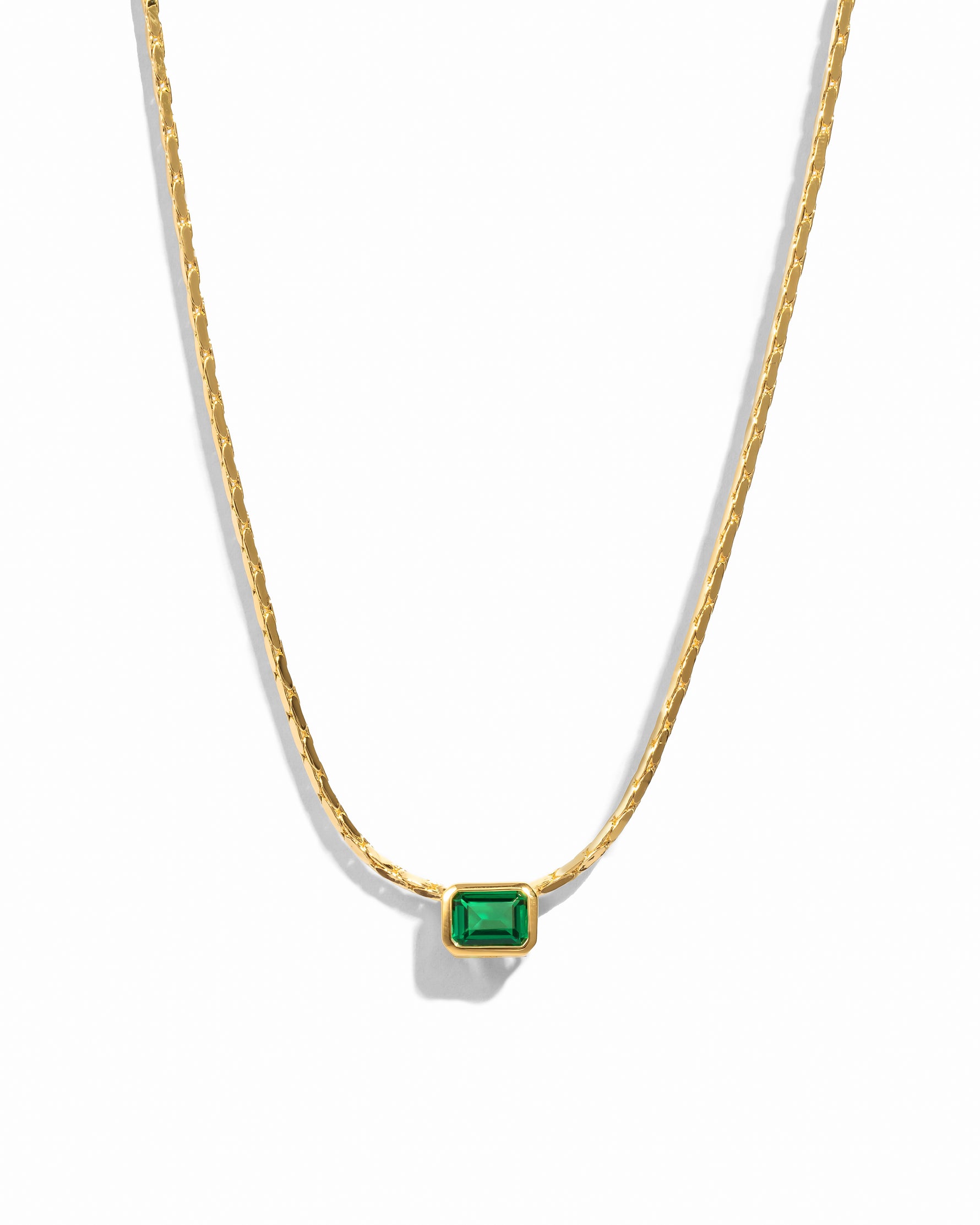 A gold-colored necklace featuring a single emerald-cut green stone set in a bezel on a chain link.