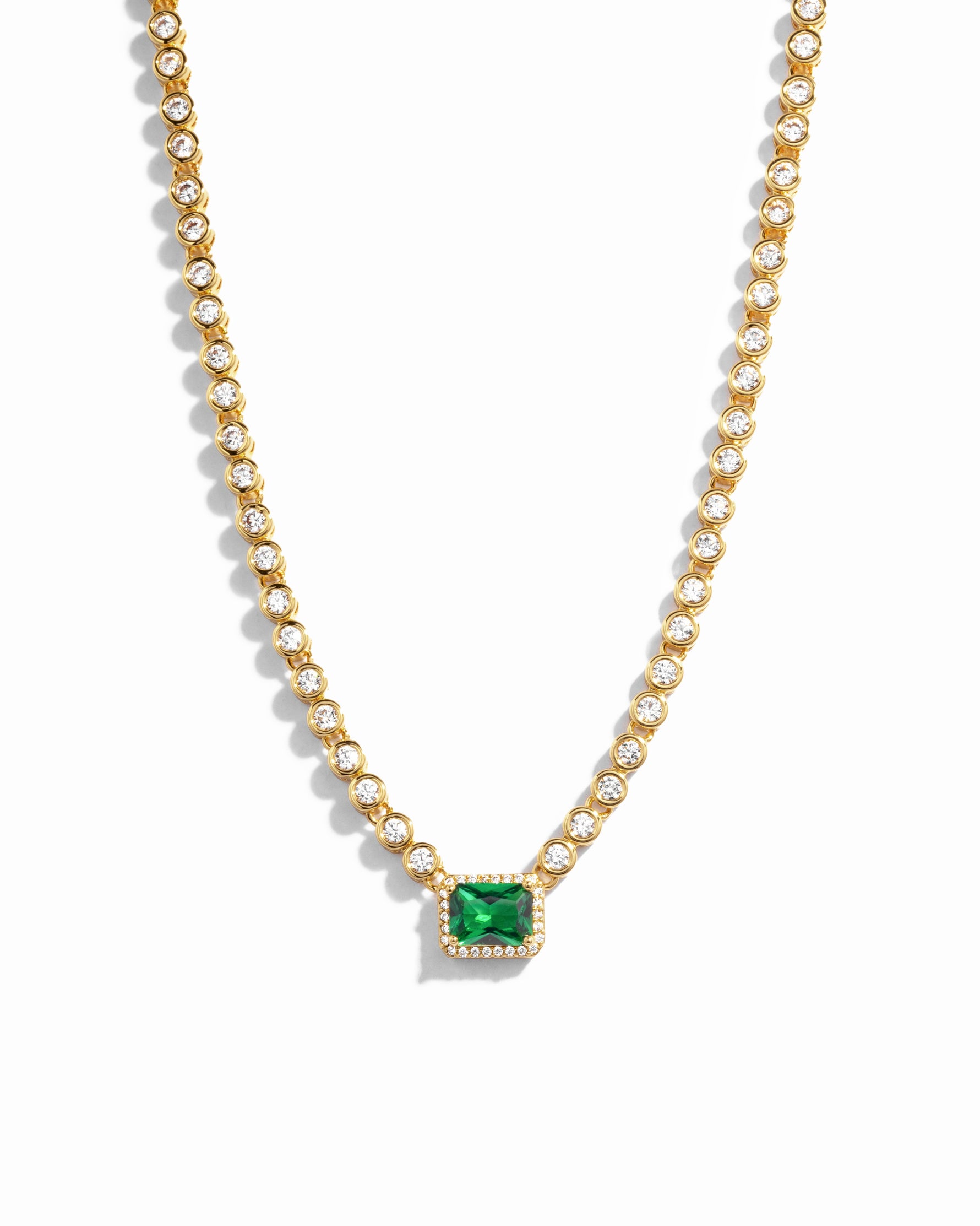 Emerald Tennis Necklace in gold, with emerald pendant surrounded by tiny diamonds on a white background
