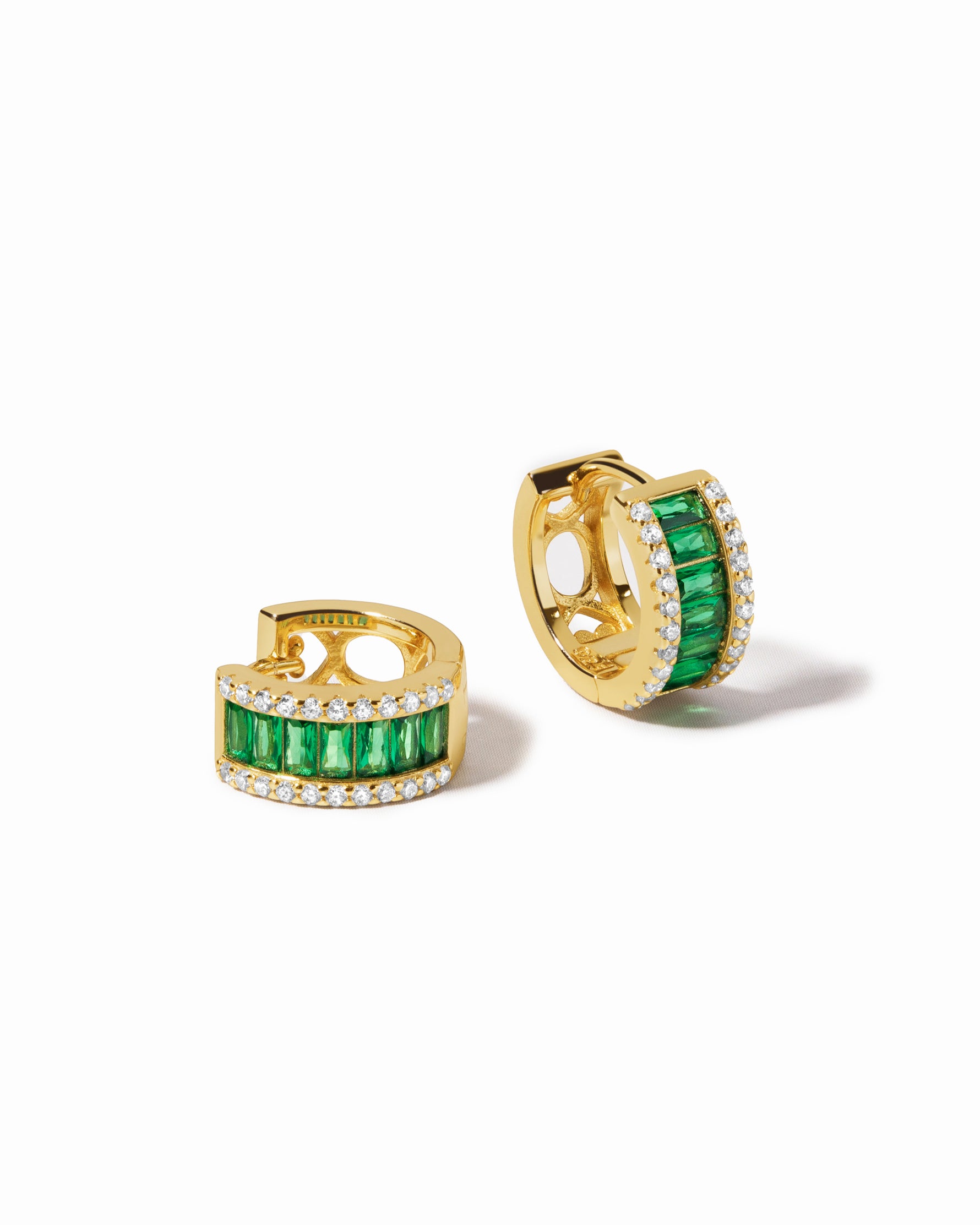 Gold huggie earrings with emerald green gemstones on a white background