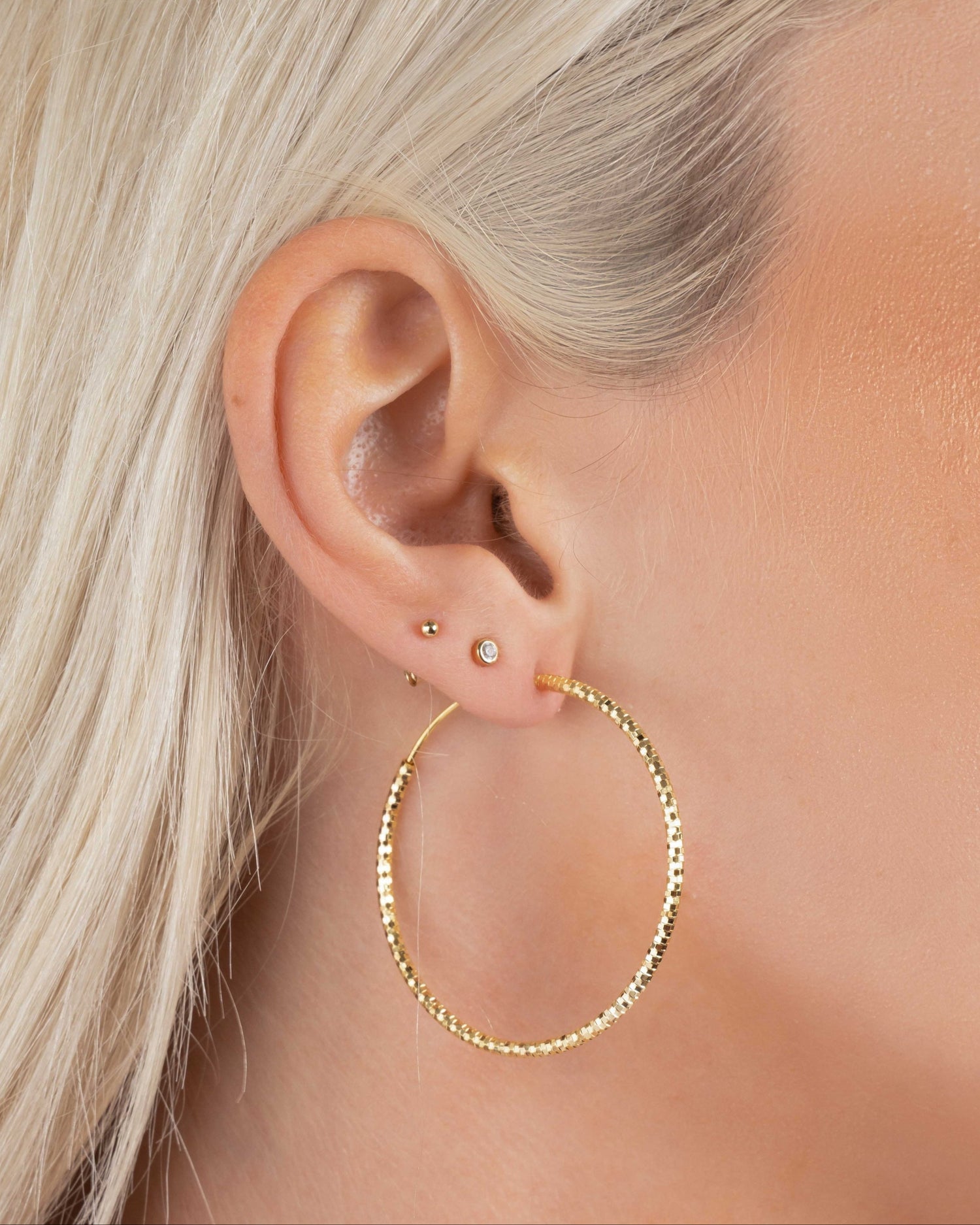 Model wearing 40mm gold hoop earrings, paired with bezel stud and ball stud earrings for a versatile ear stack.