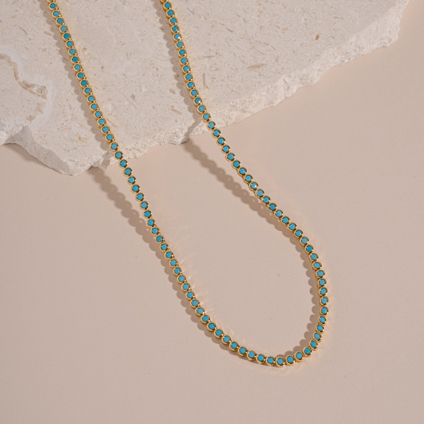 flatlay of gold tennis necklace with turquoise stones and a round bezel design