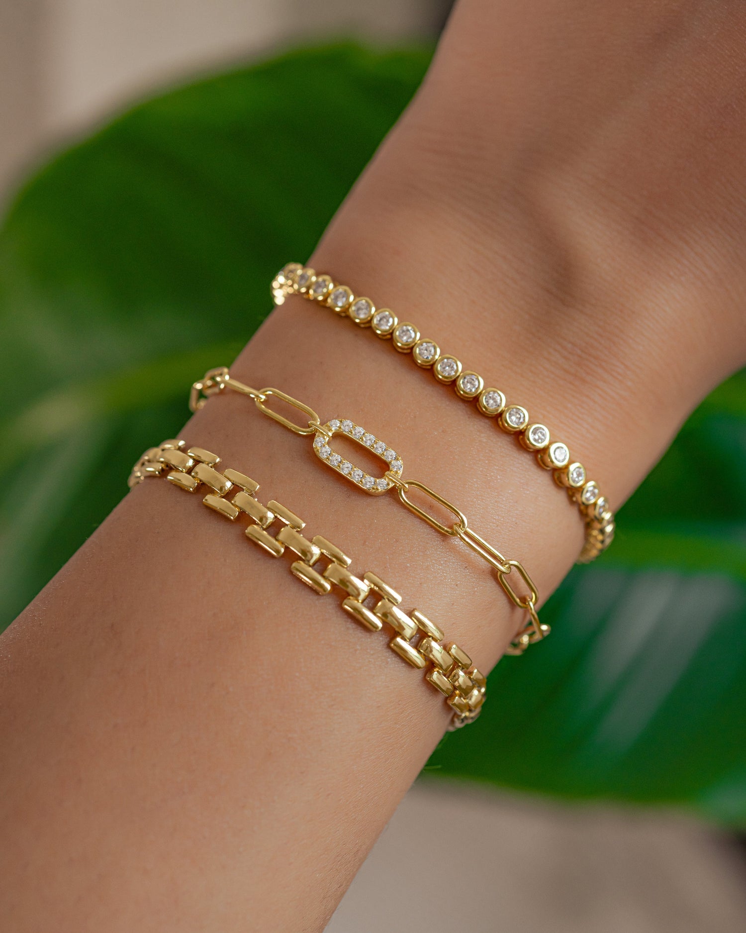 model wearing gold bracelet stack including a chain link bracelet, a paperclip bracelet with a cz charm, and a round bezel tennis bracelet