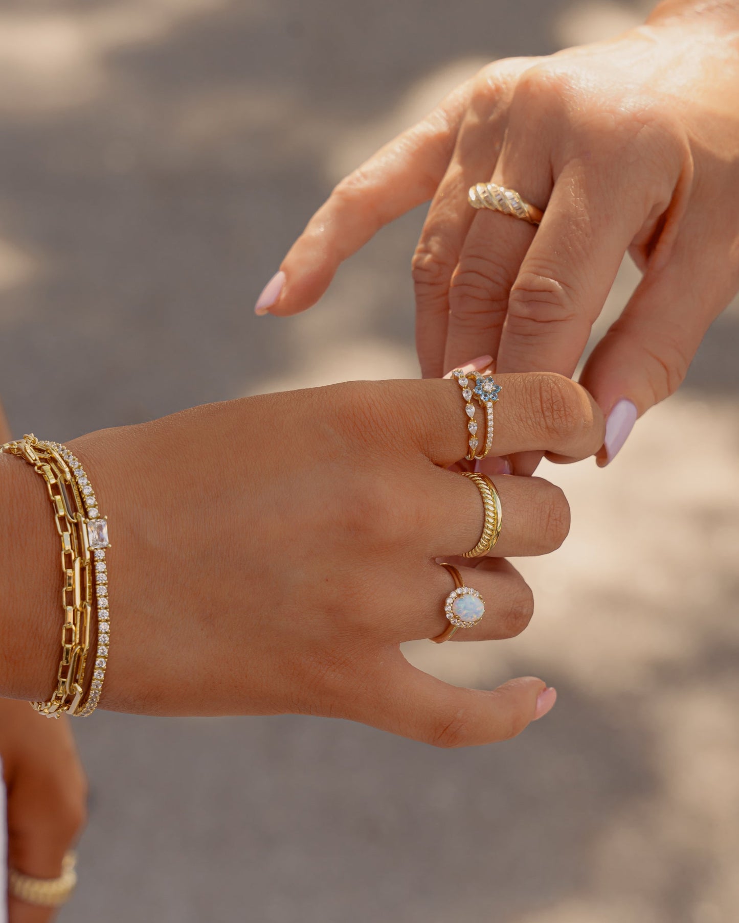model holding hands with another model, both wearing gold ring stacks featuring an opal oval solitaire statement ring