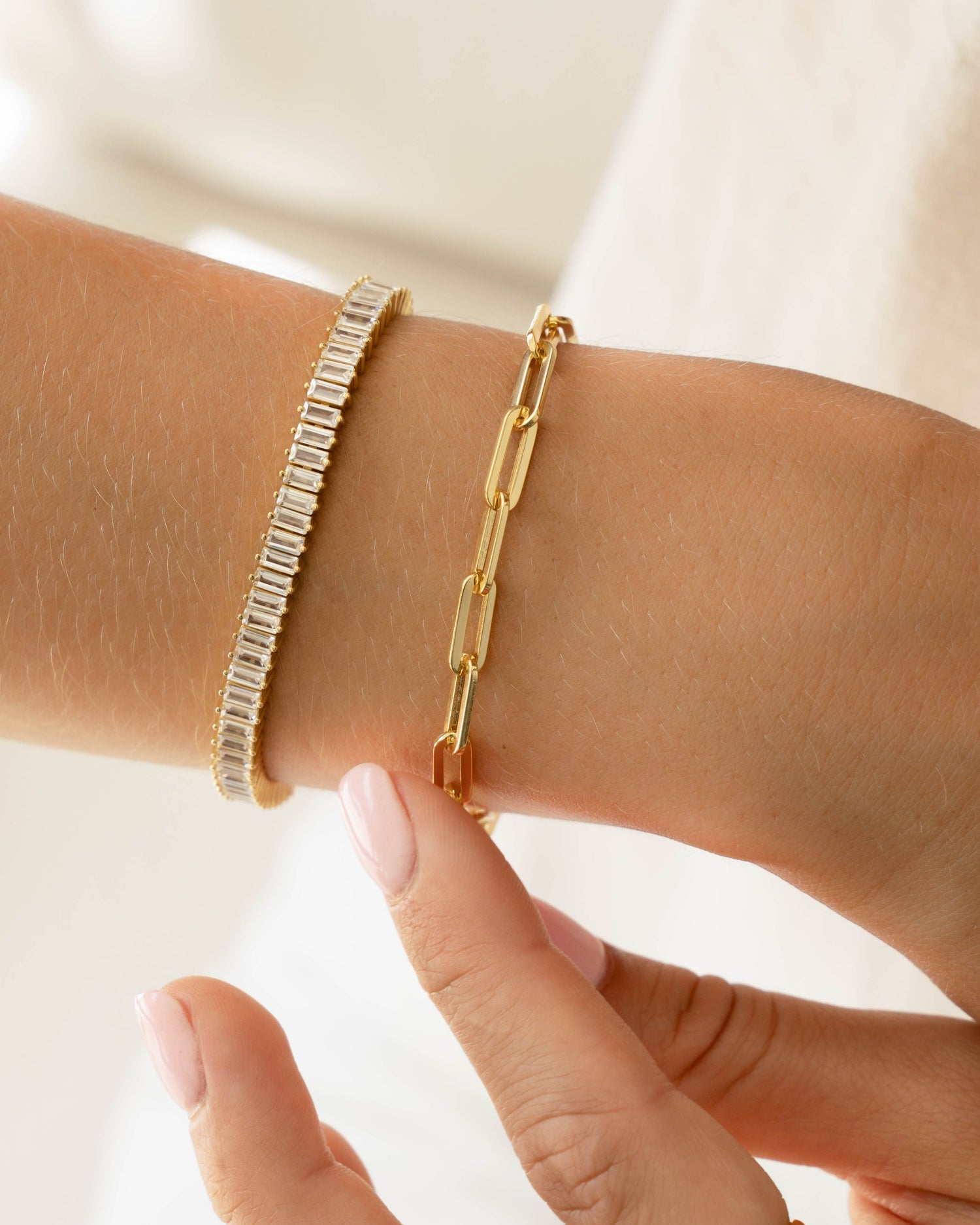 model wearing gold bracelets featuring gold paperclip bracelet and gold baguette tennis necklace