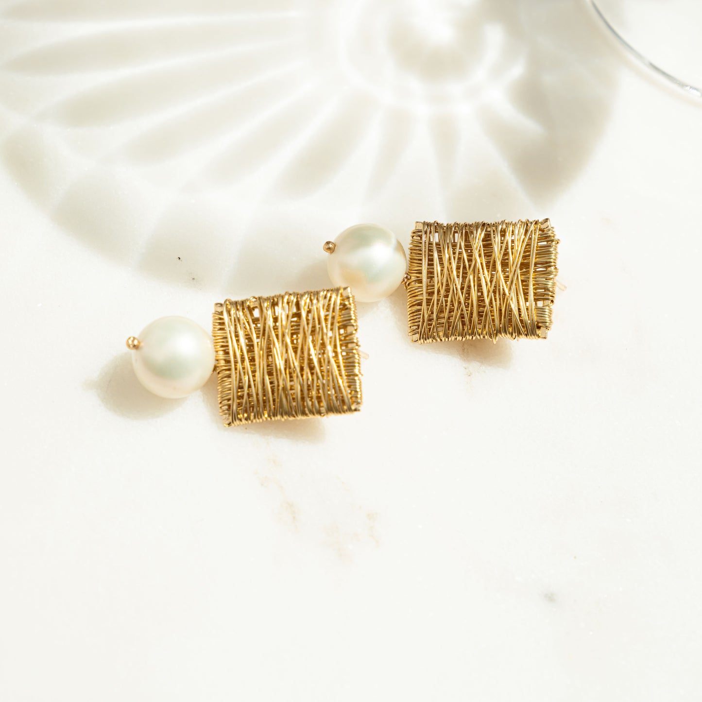 closeup image of pearl charm earrings featuring a square earring