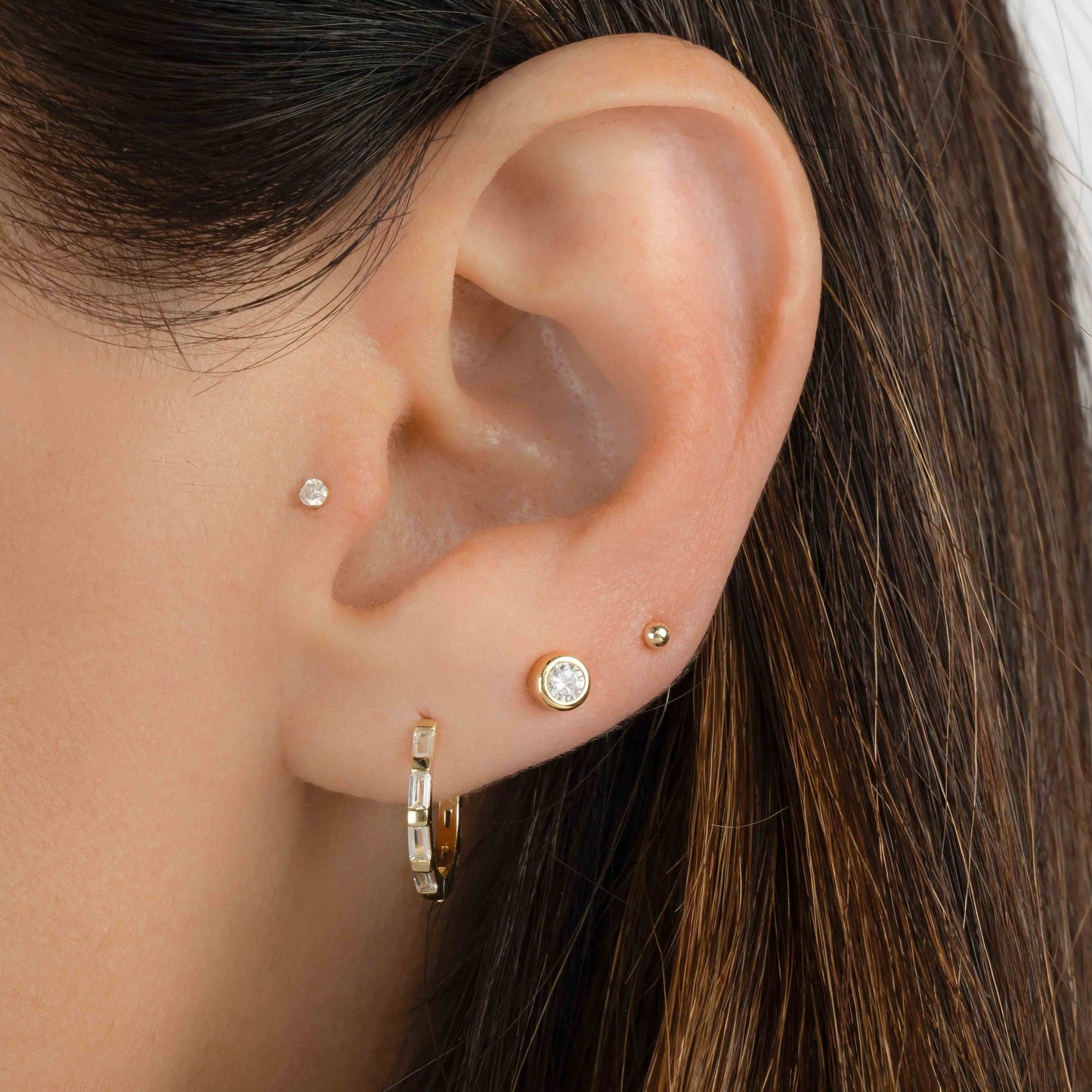 Model wearing gold earrings featuring small baguette hoops