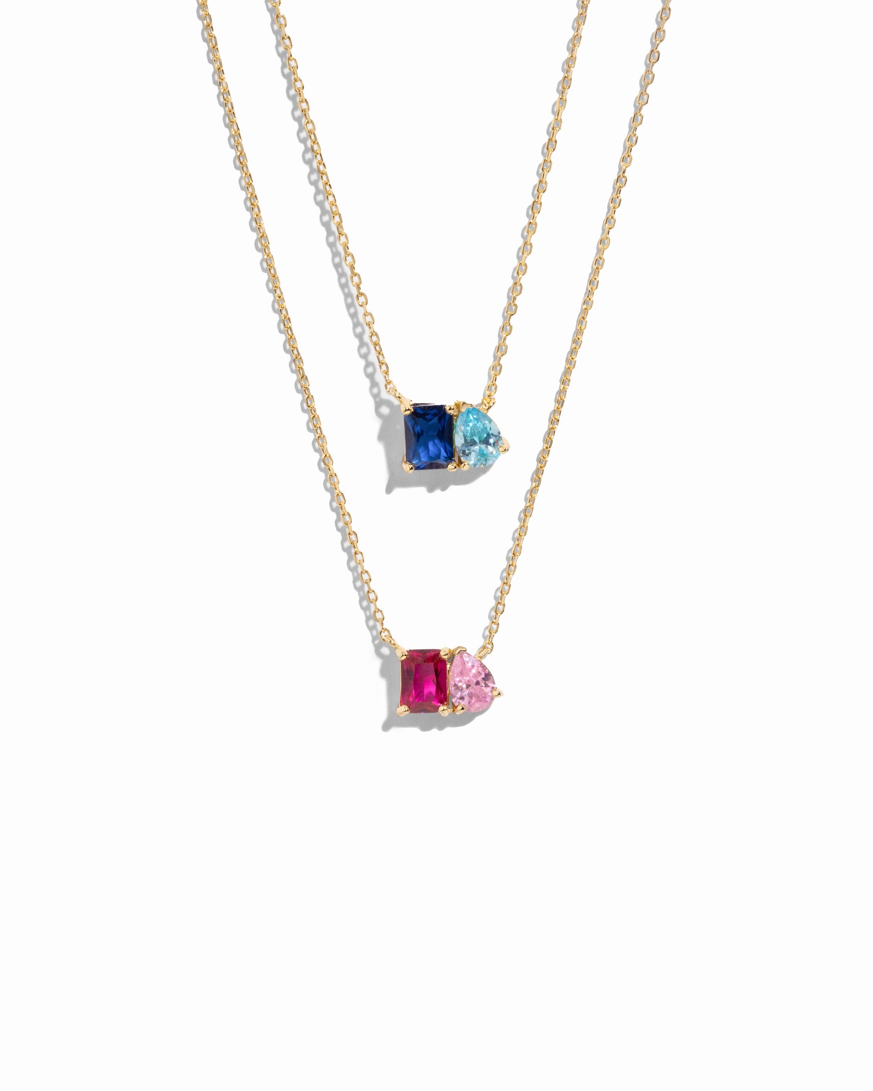 Two gold necklaces with custom birthstone gemstone pendants on a white background,
