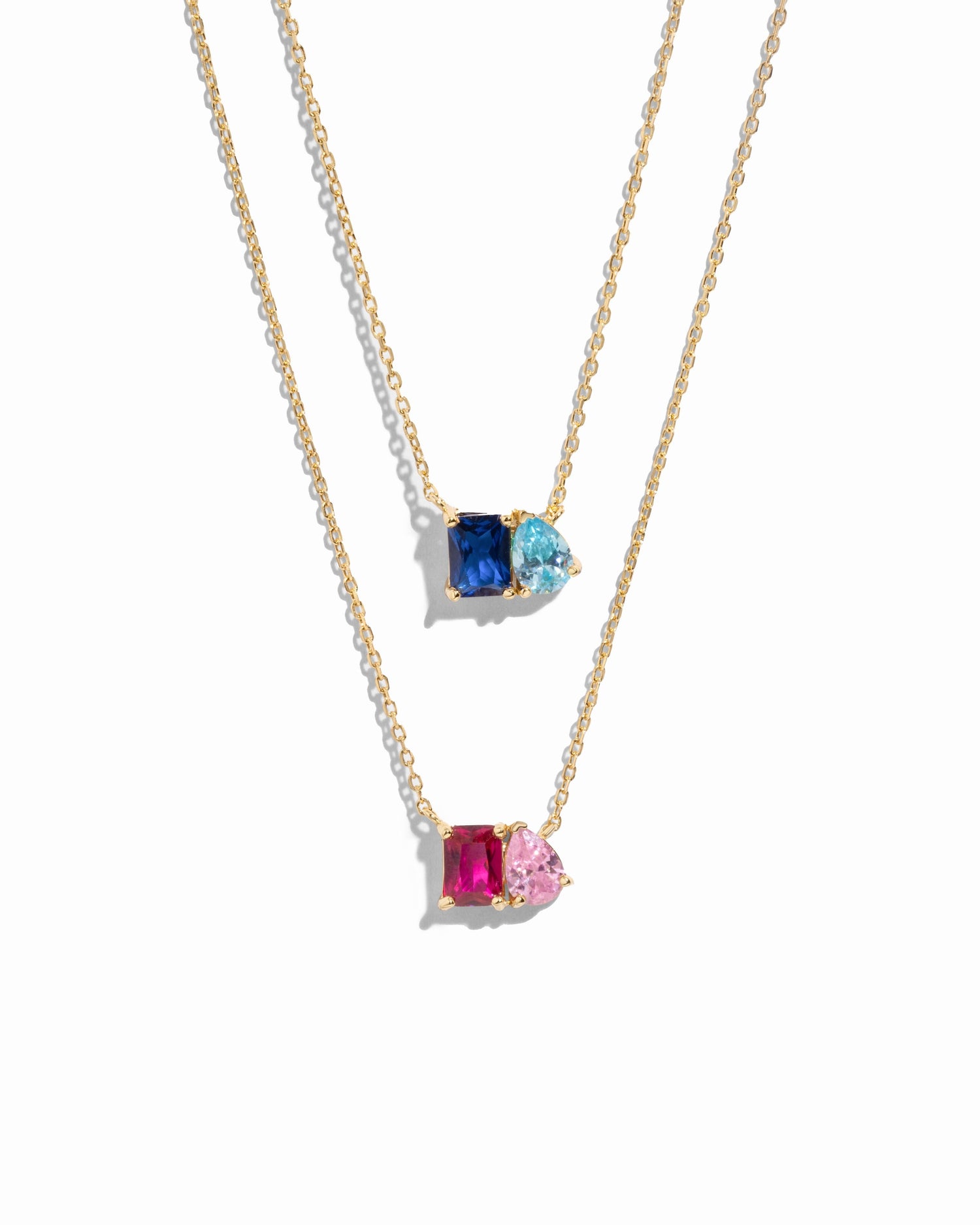 Two gold necklaces with custom birthstone gemstone pendants on a white background,