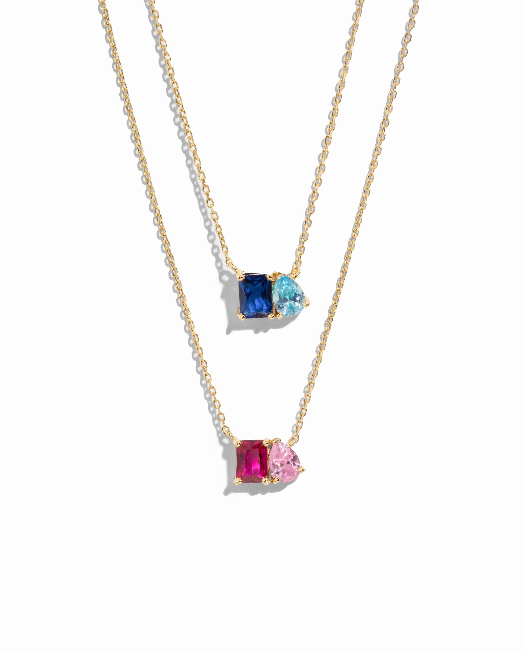 Two gold necklaces with custom birthstone gemstone pendants on a white background,