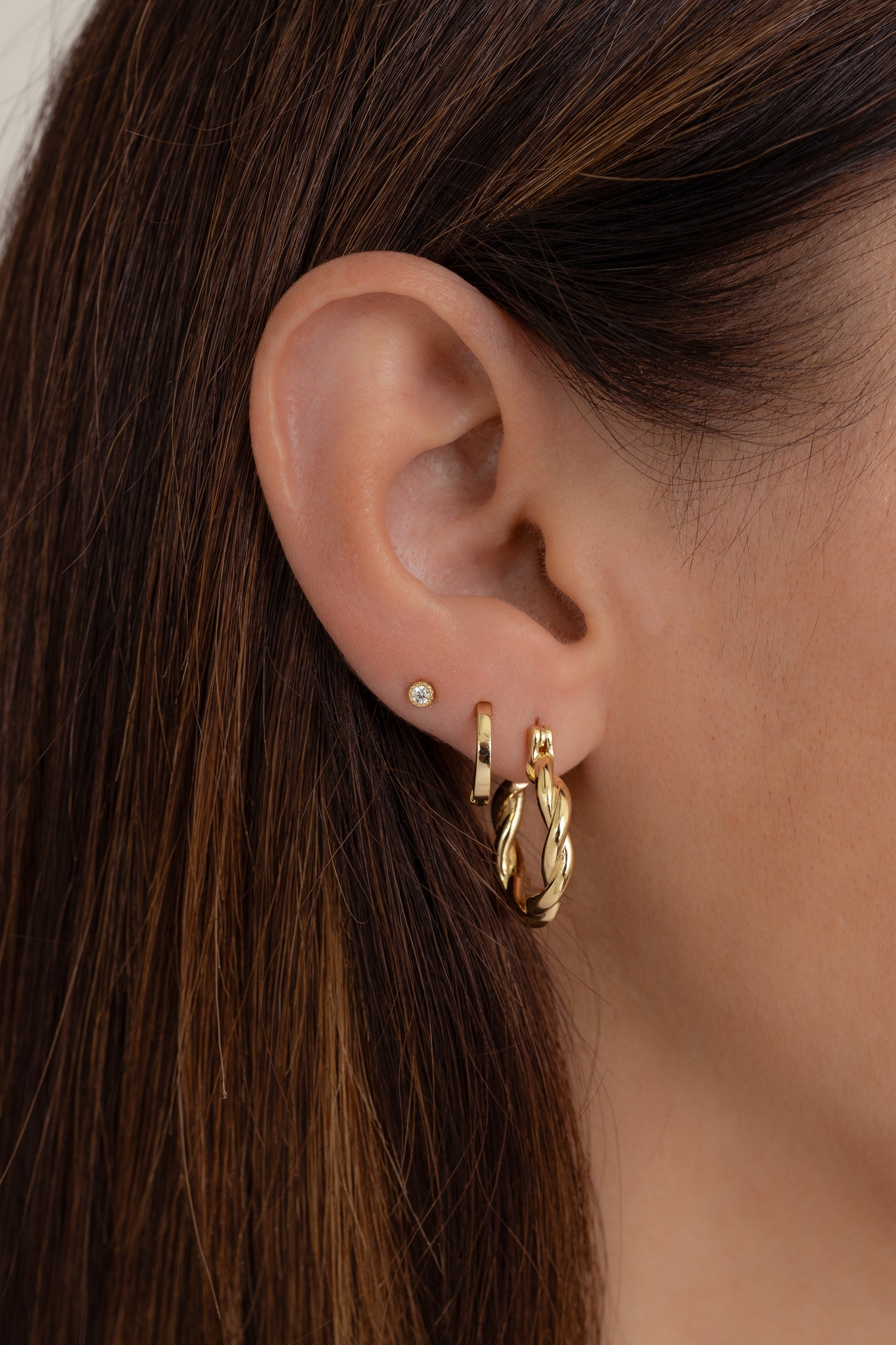 Model wearing gold chunky spiral hoop earrings with minimalist huggies and a bezel stud.
