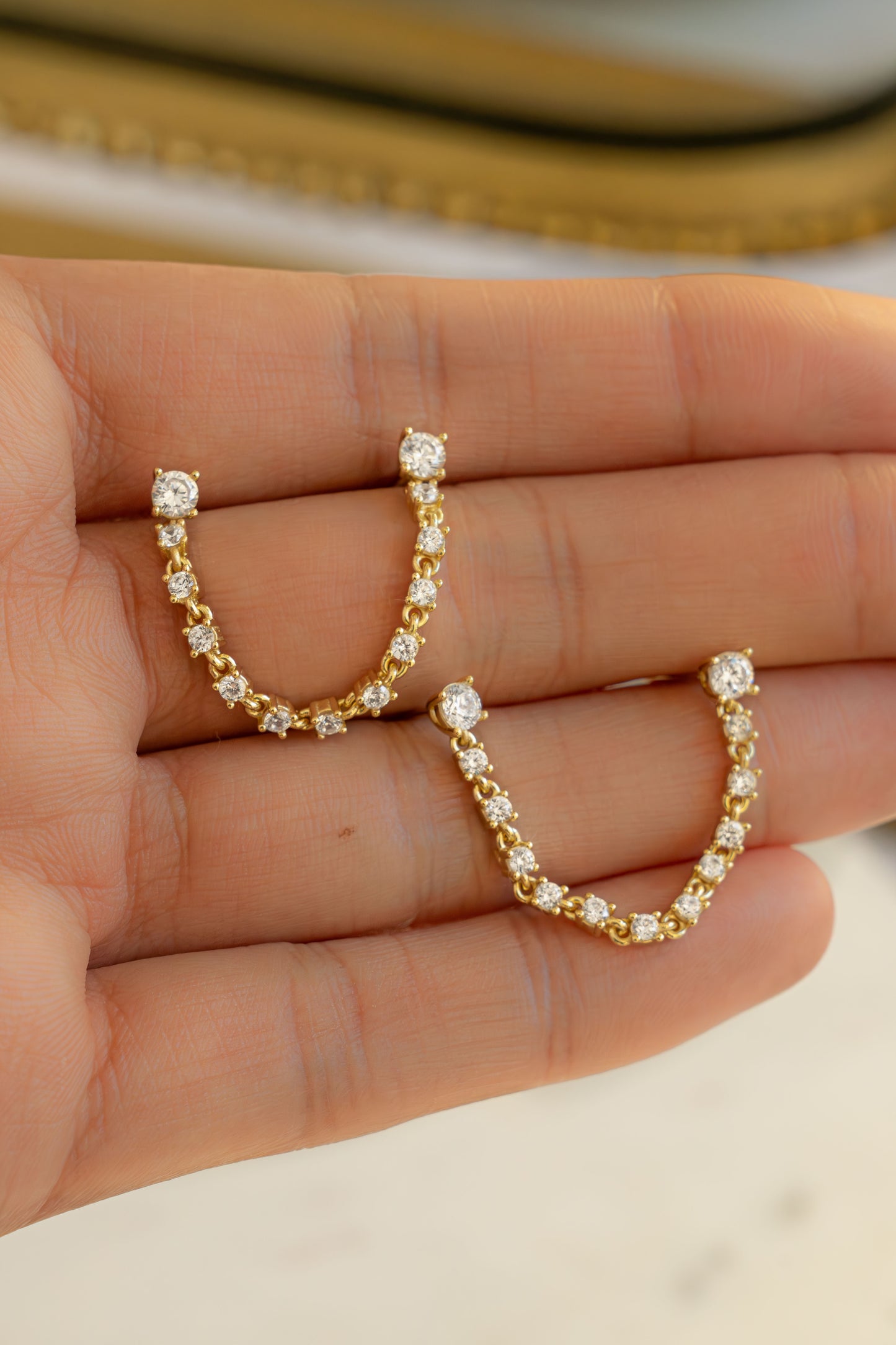 held on hand, a close up of a pair of diamond-studded gold earrings for Double piercing