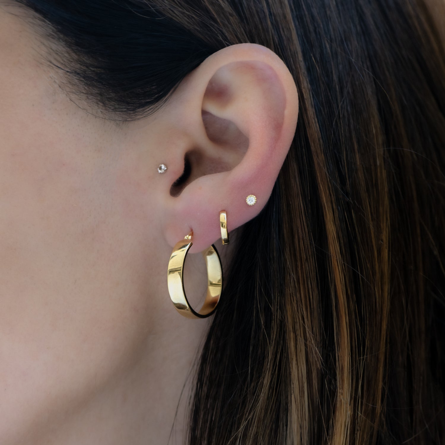 Model wearing chunky gold hoops, minimalist huggies, and a bezel stud earring.