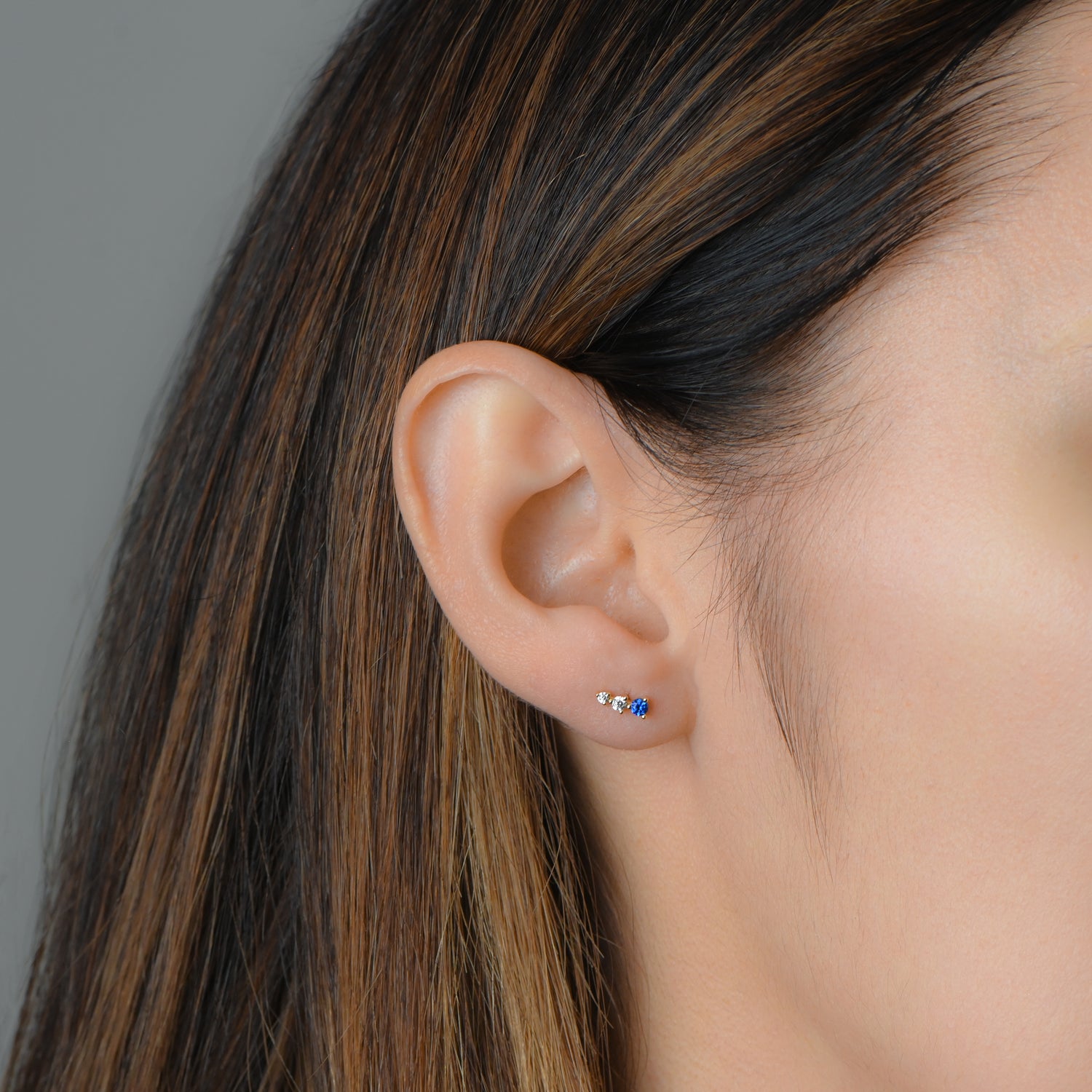 Model wearing gold ear climber studs with sapphire and diamond stones.