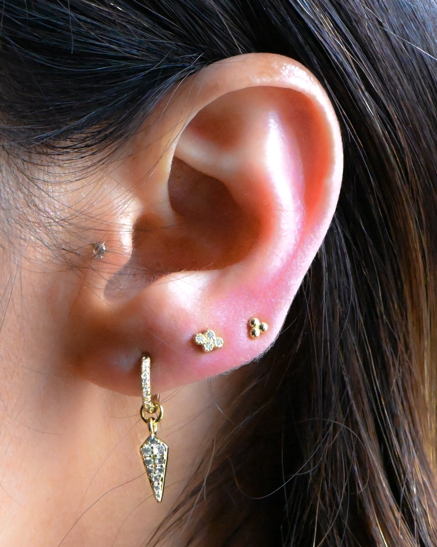 Model wearing tiny minimalist spike charm earring with 4 ball stud earring and three ball stud earring in her second and third piercing.