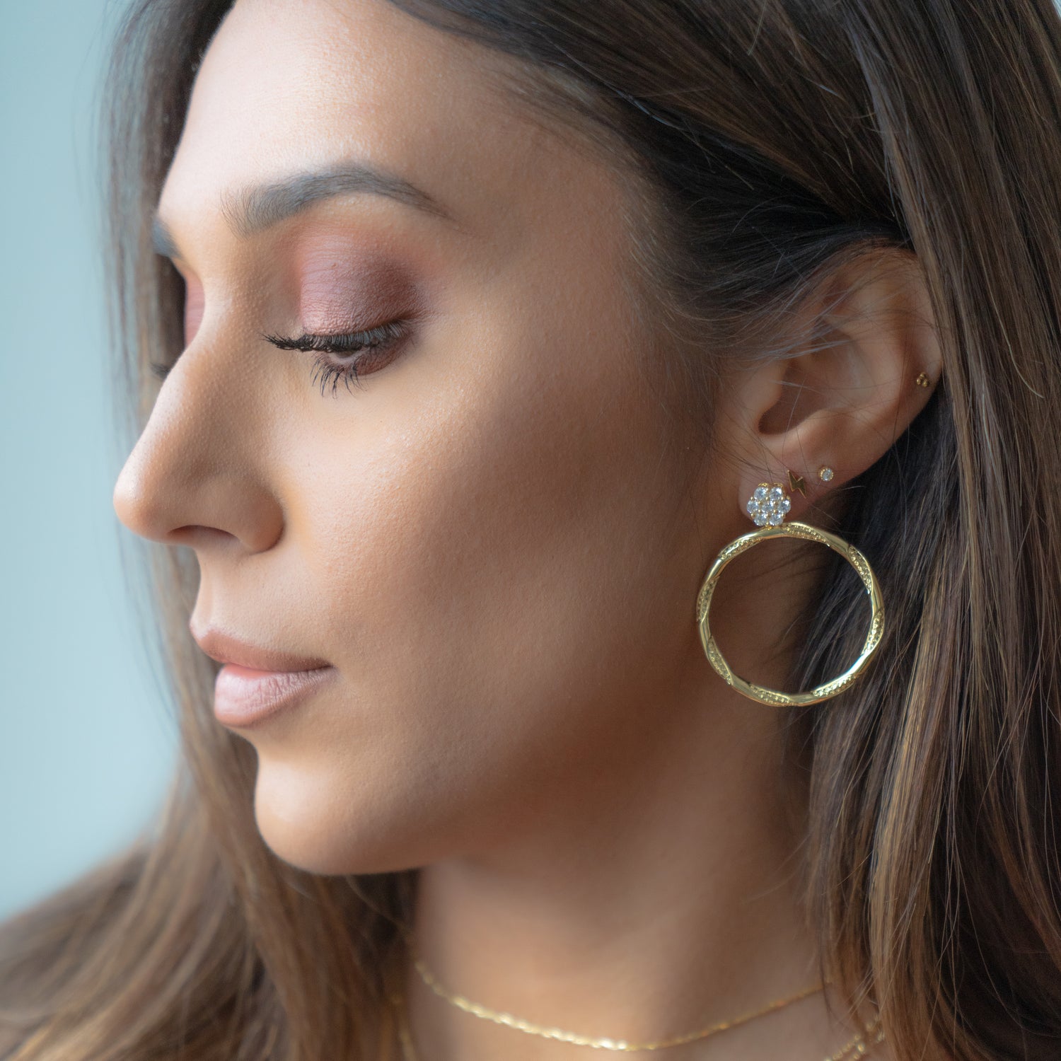 Model wearing gold diamond circle earring with textured hoop, lightning bolt stud, and diamond stud,