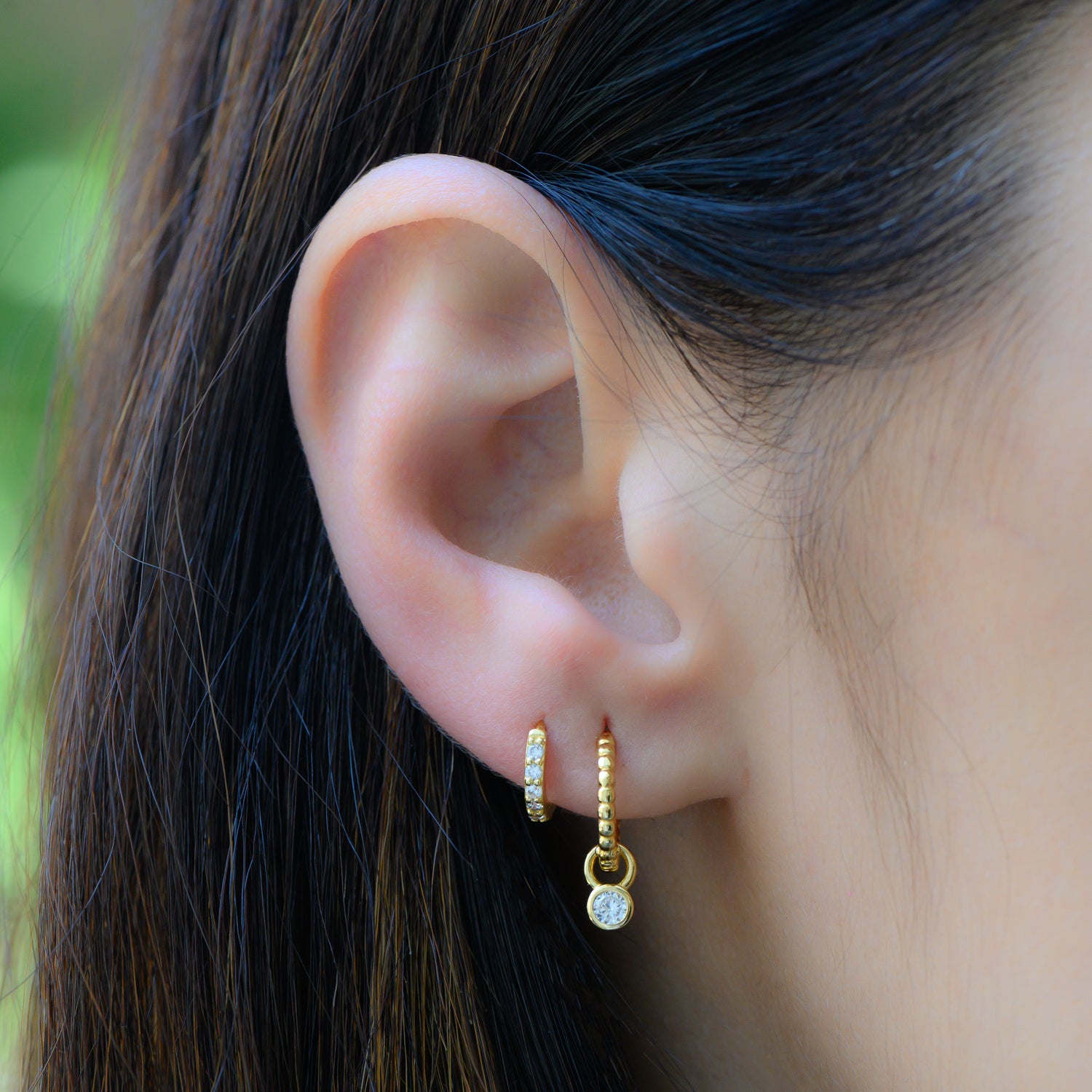 Model wearing dainty gold huggie earrings with bezel diamond charm.