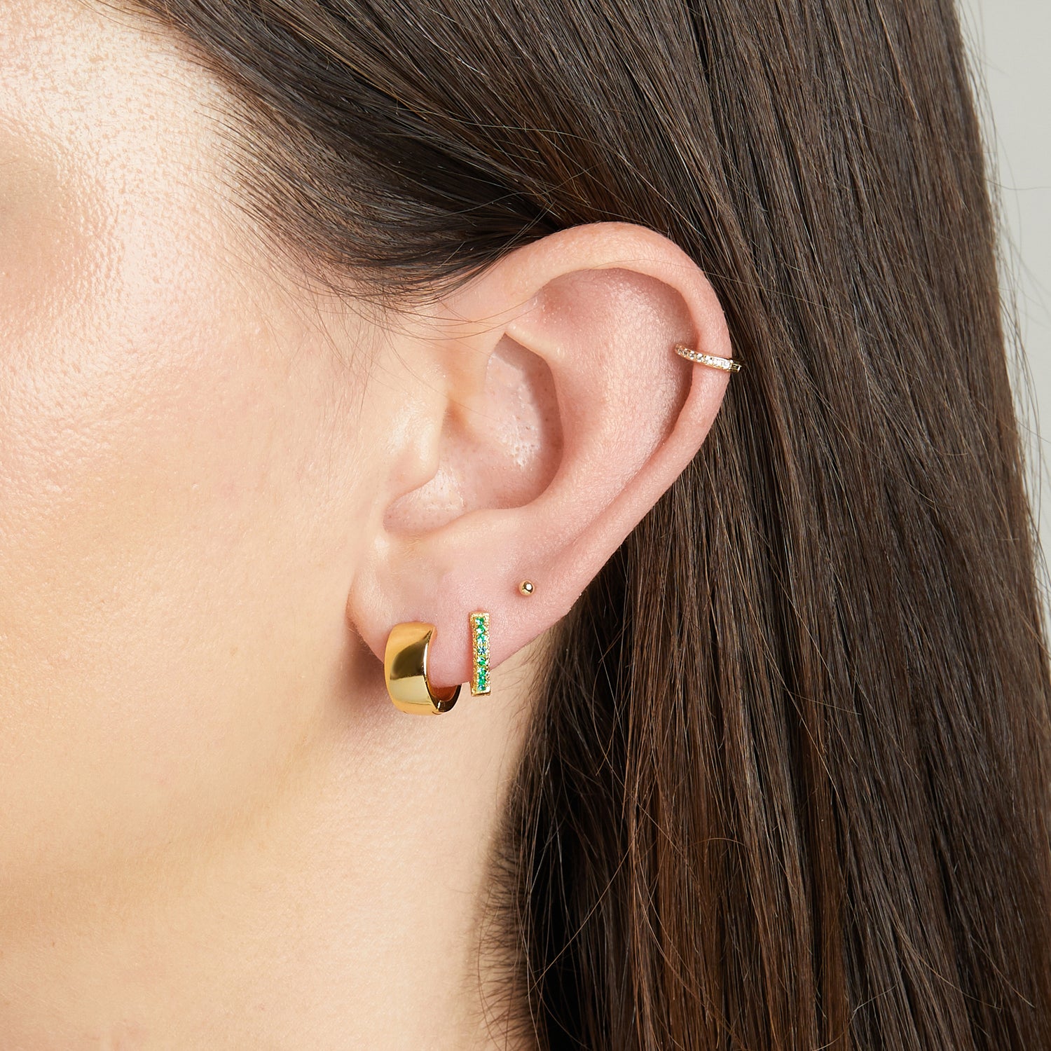 Model wearing chunky gold hoops and emerald pavé earrings.
