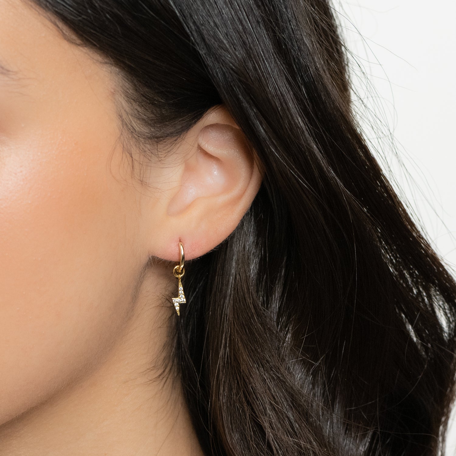 Model wearing dainty gold huggies with lightning bolt charm.