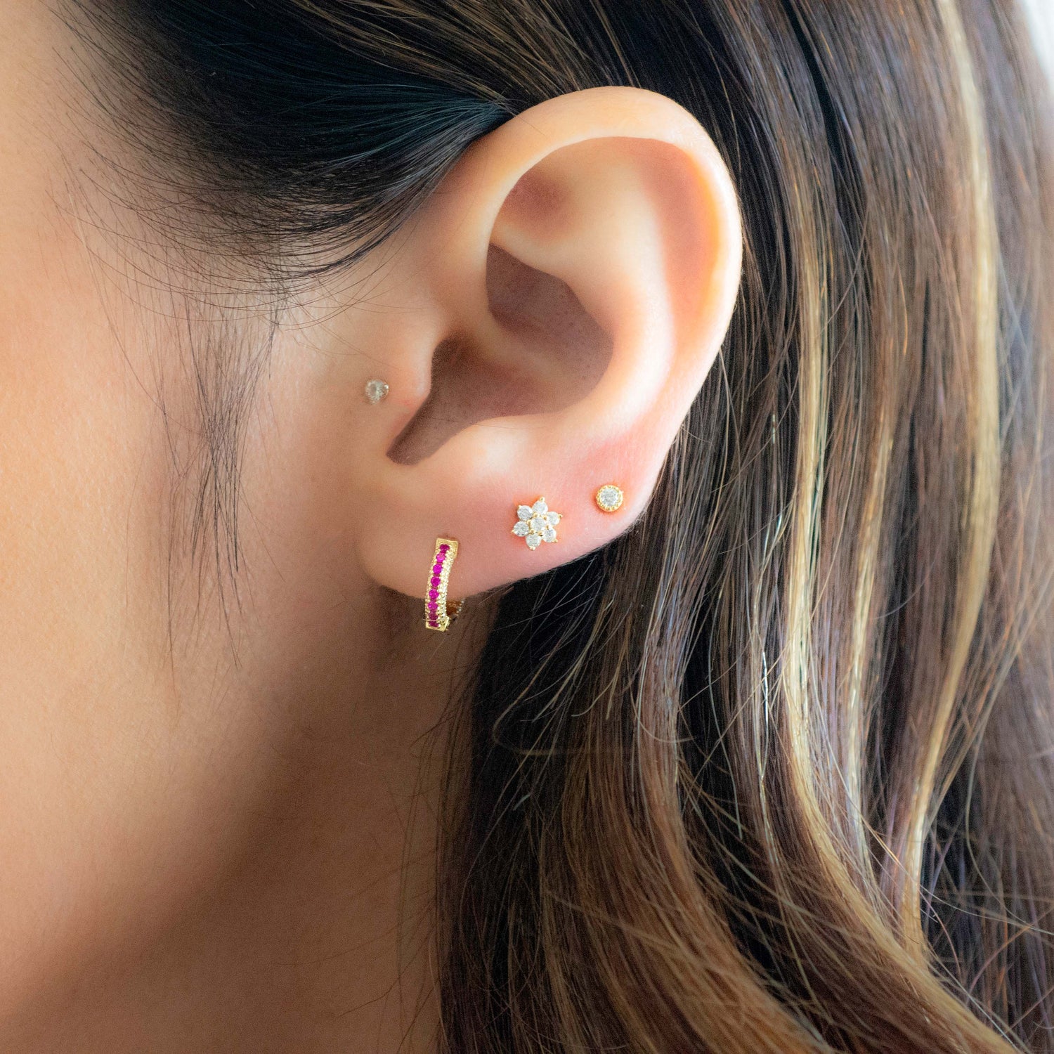 Model wearing gold pavé huggie earrings with ruby CZ's and diamond flower studs.