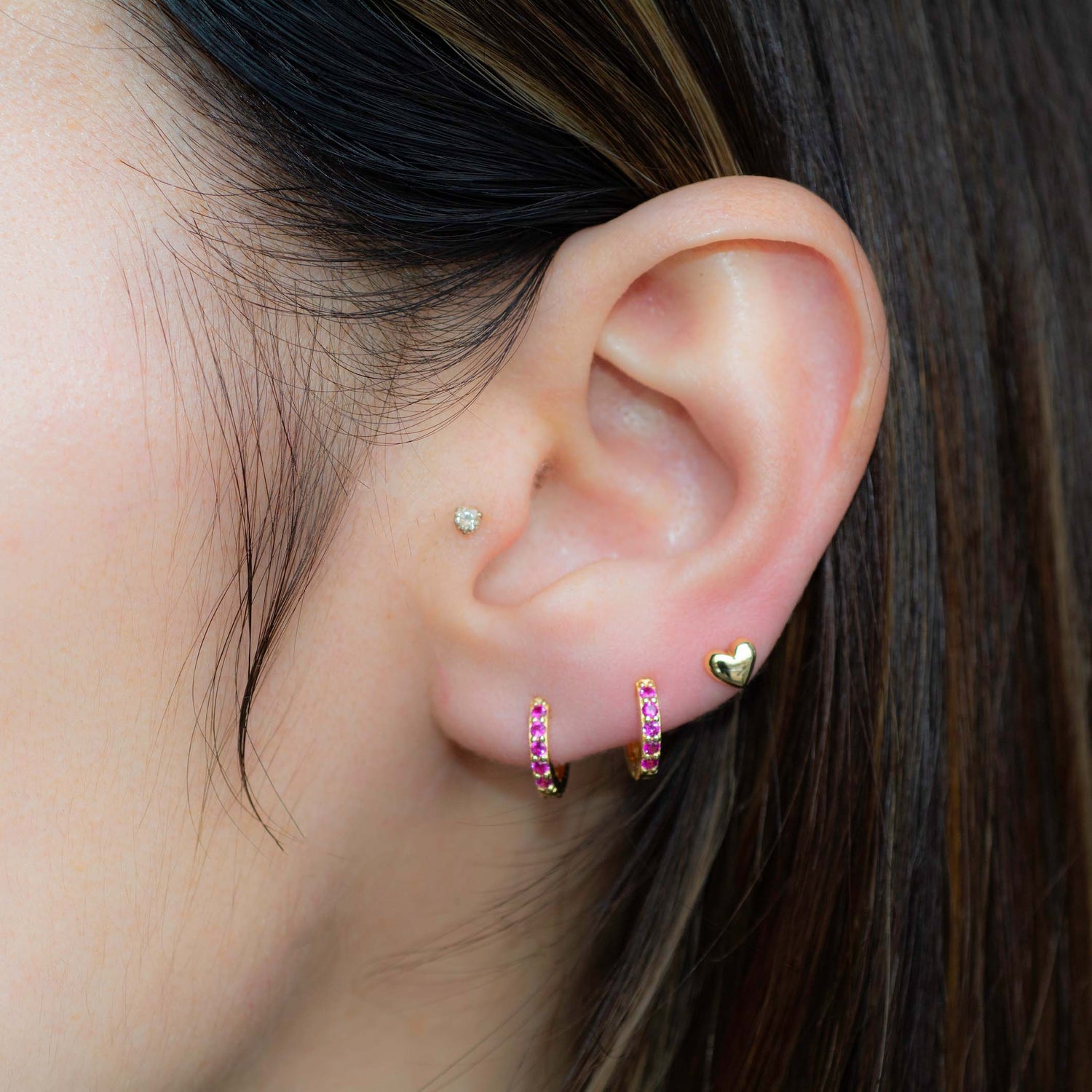 Model wearing gold dainty ruby huggies and a heart stud,