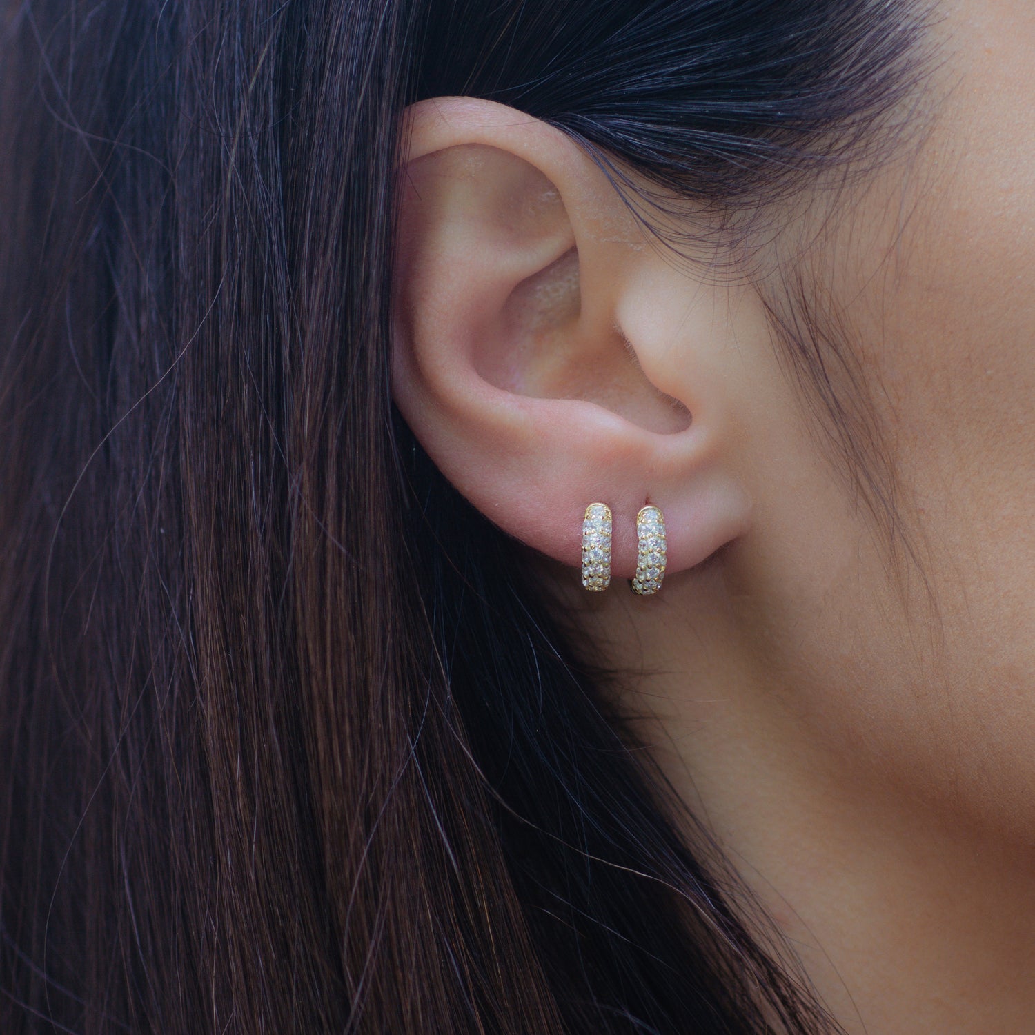 Two gold huggie diamond hoop earrings on model