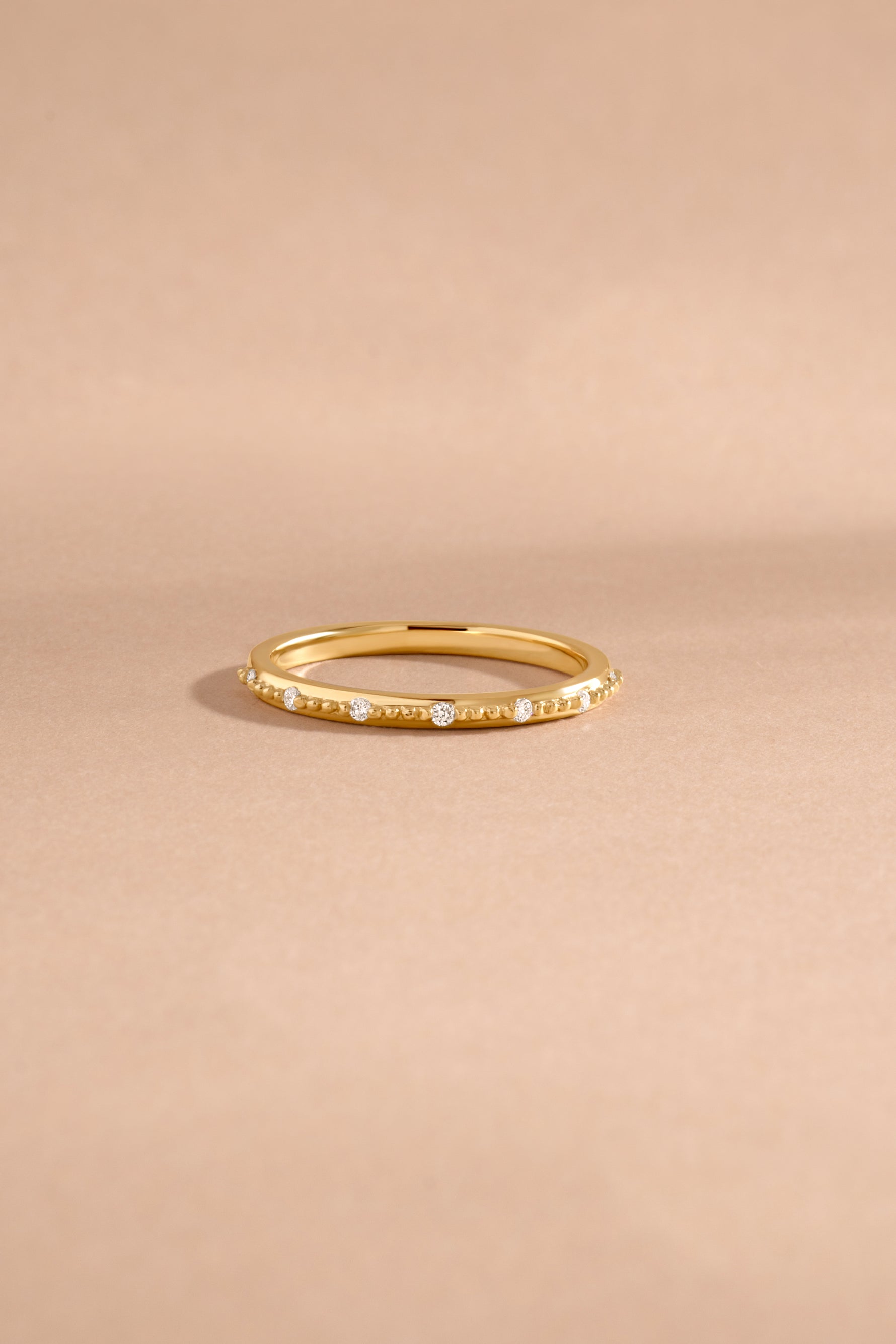 Thin 14K solid gold ring featuring seven lab grown diamonds on beige background