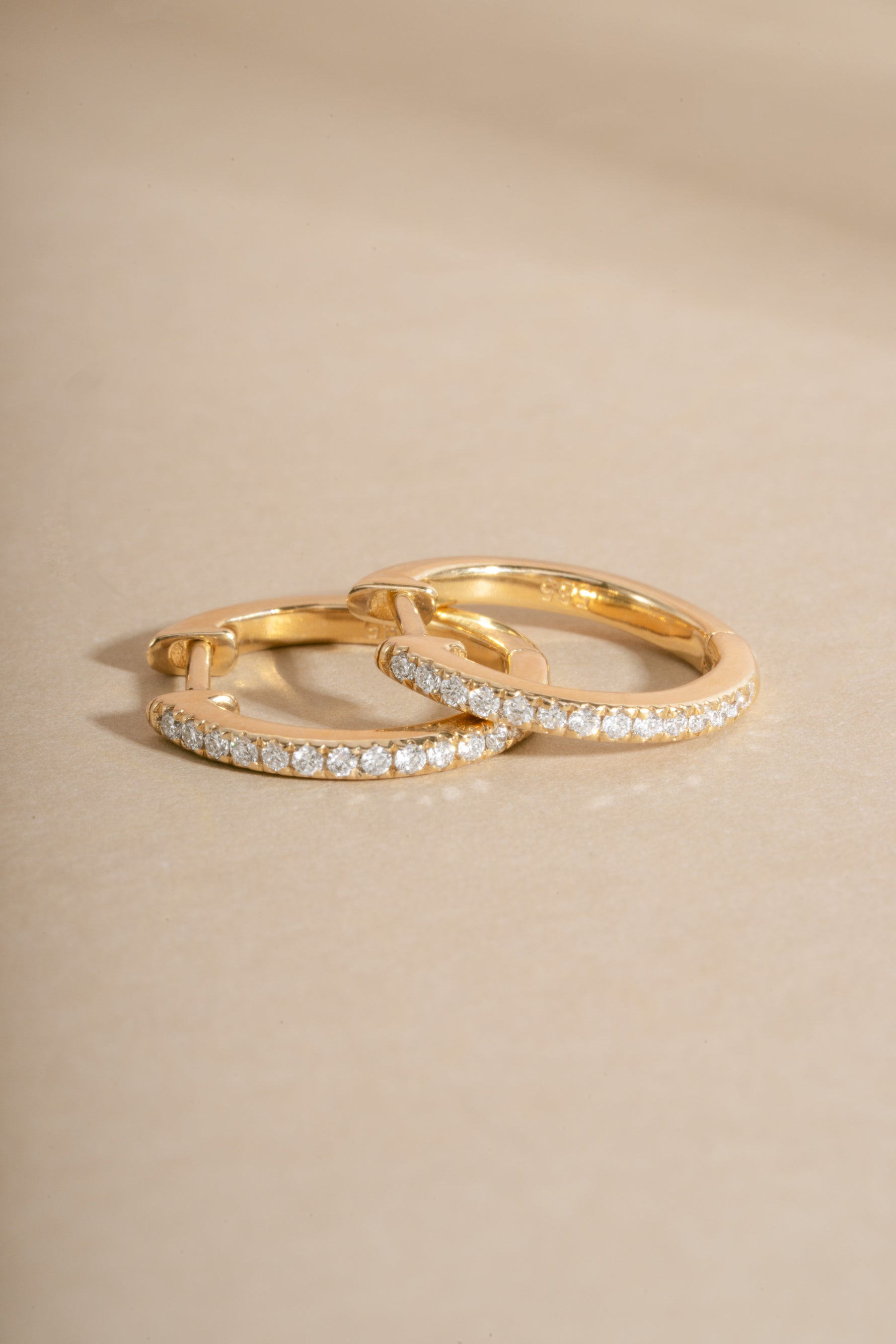 Close-up of 14K solid gold 11mm pavé lab-grown diamond huggie earrings by Sami Jewels on a flat lay.
