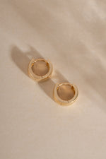 Chunky solid gold hoop earrings on neutral background