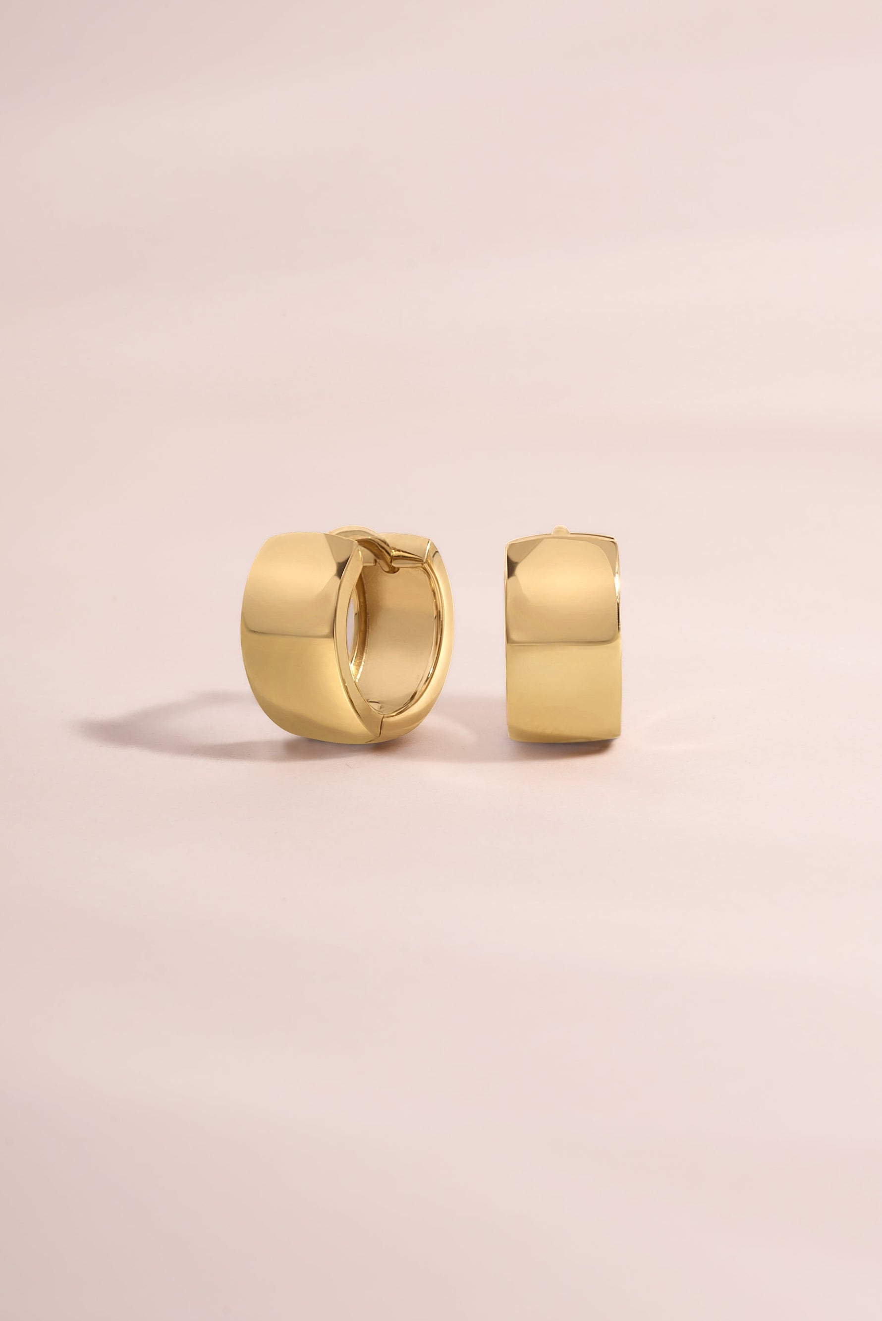 Chunky 14K solid gold hoop earrings on a light pink background