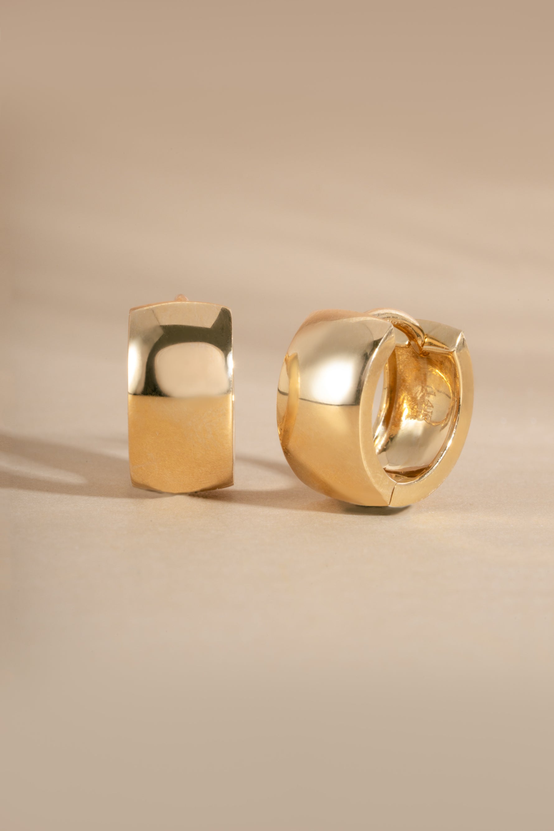 Solid gold hoop earrings on a beige background
