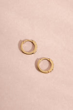 Pair of 14K solid gold 7mm diamond huggie earrings flat lay on soft pink background