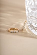 Close-up of 14K solid gold 7mm diamond huggie earrings with lab grown diamonds on neutral beige background