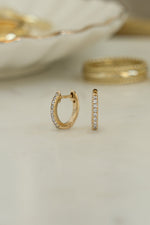 Close-up of 14K solid gold 8mm pavé diamond huggie earrings with lab grown diamonds with blurred background