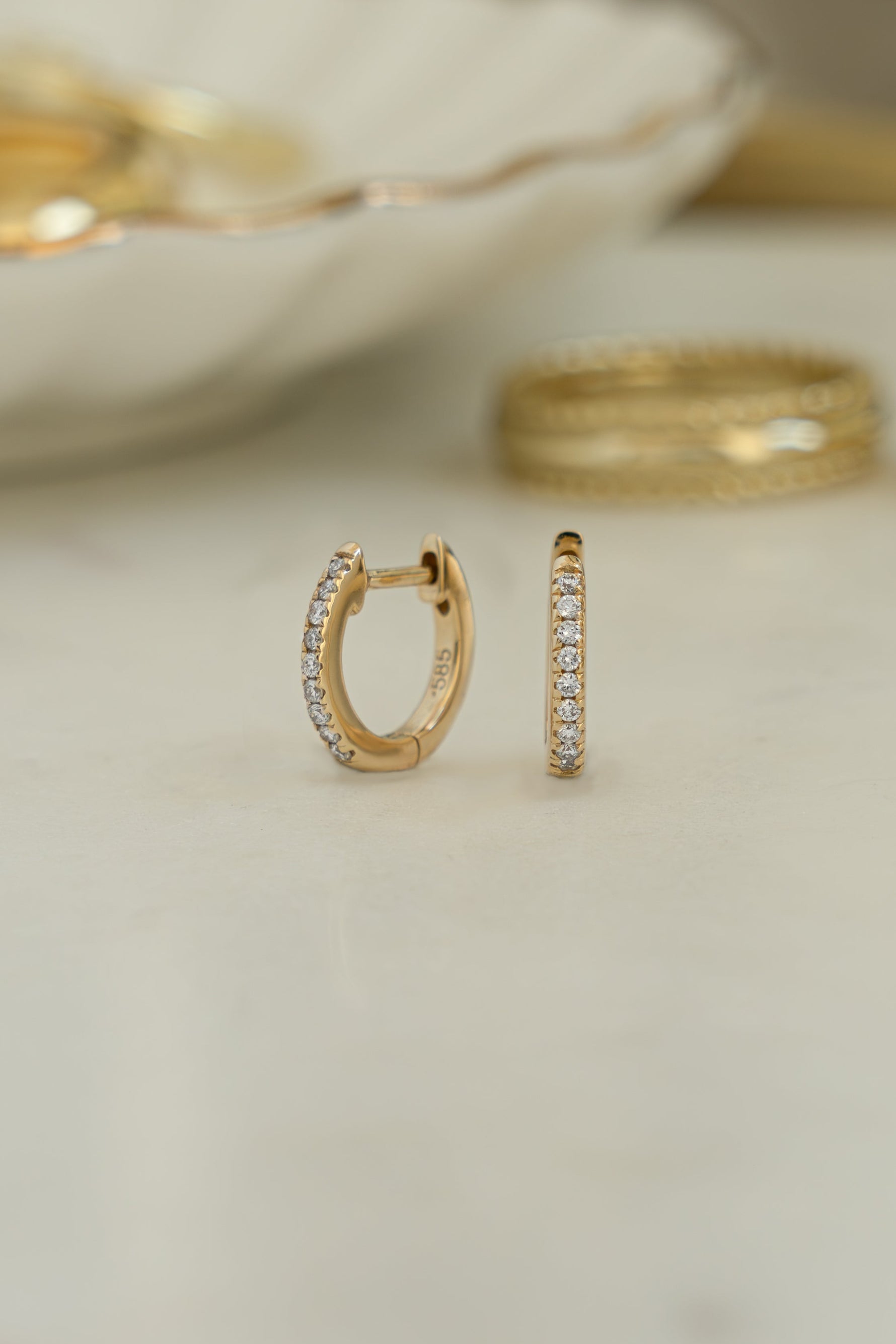 Close-up of 14K solid gold 8mm pavé diamond huggie earrings with lab grown diamonds with blurred background