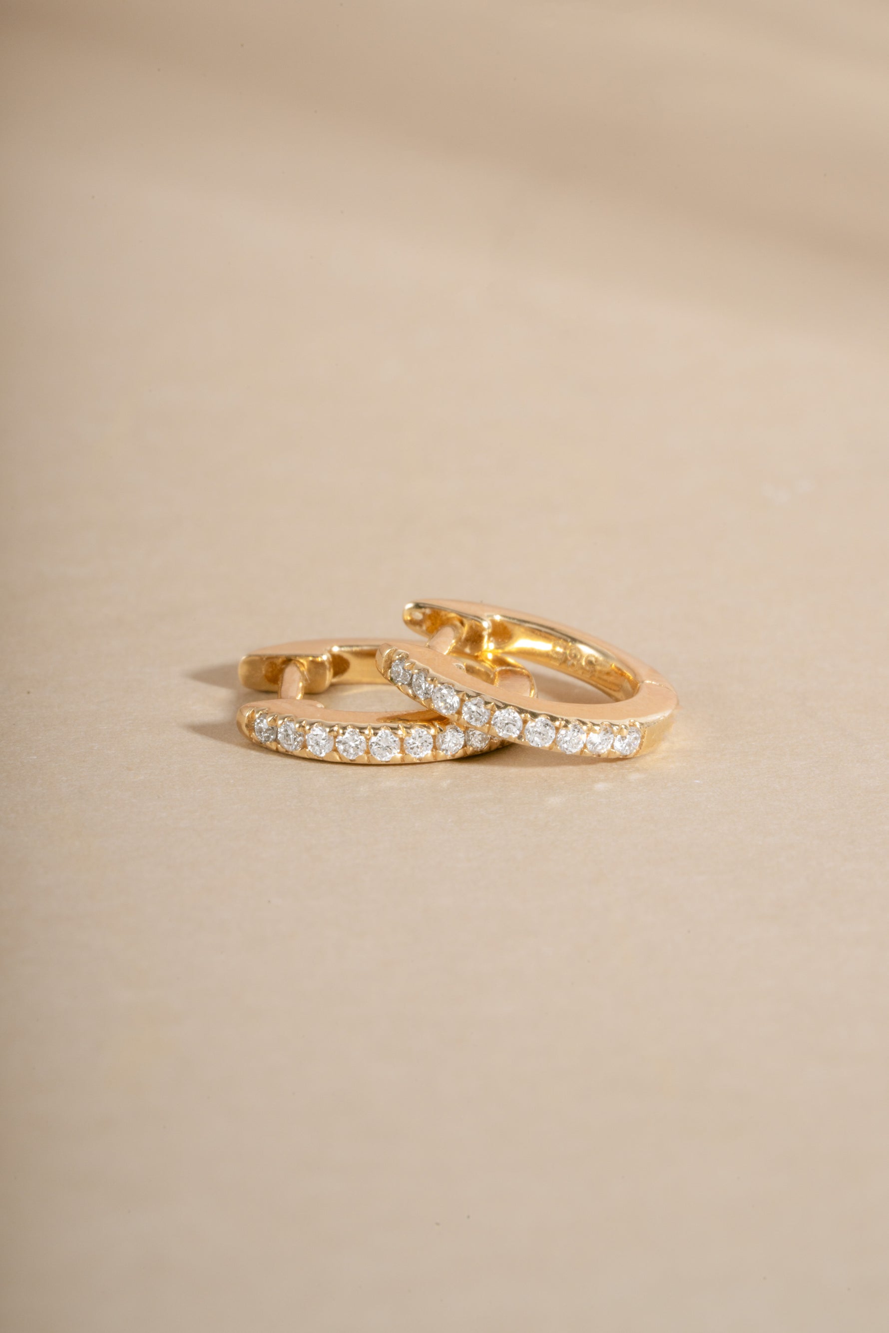 Pair of 14K solid gold diamond small hoops stacked on beige background